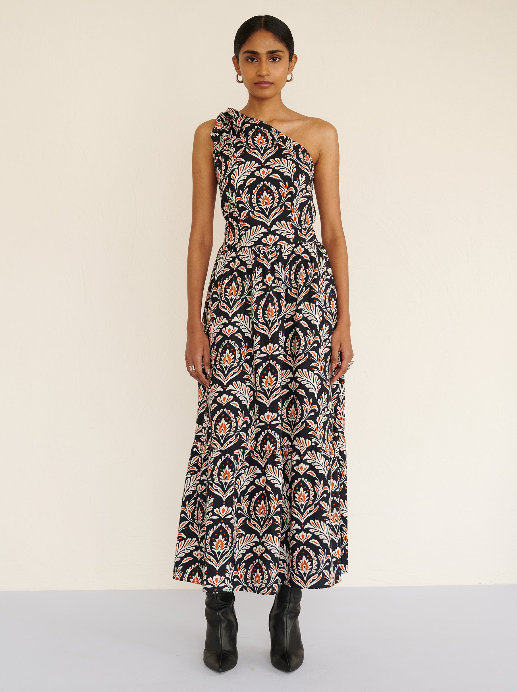 Back view of a model standing. She is wearing the Aliza full-length dress in crisp cotton poplin with the Akbar print. It is featuring an adjustable tie at the shoulder and side-seam pockets.