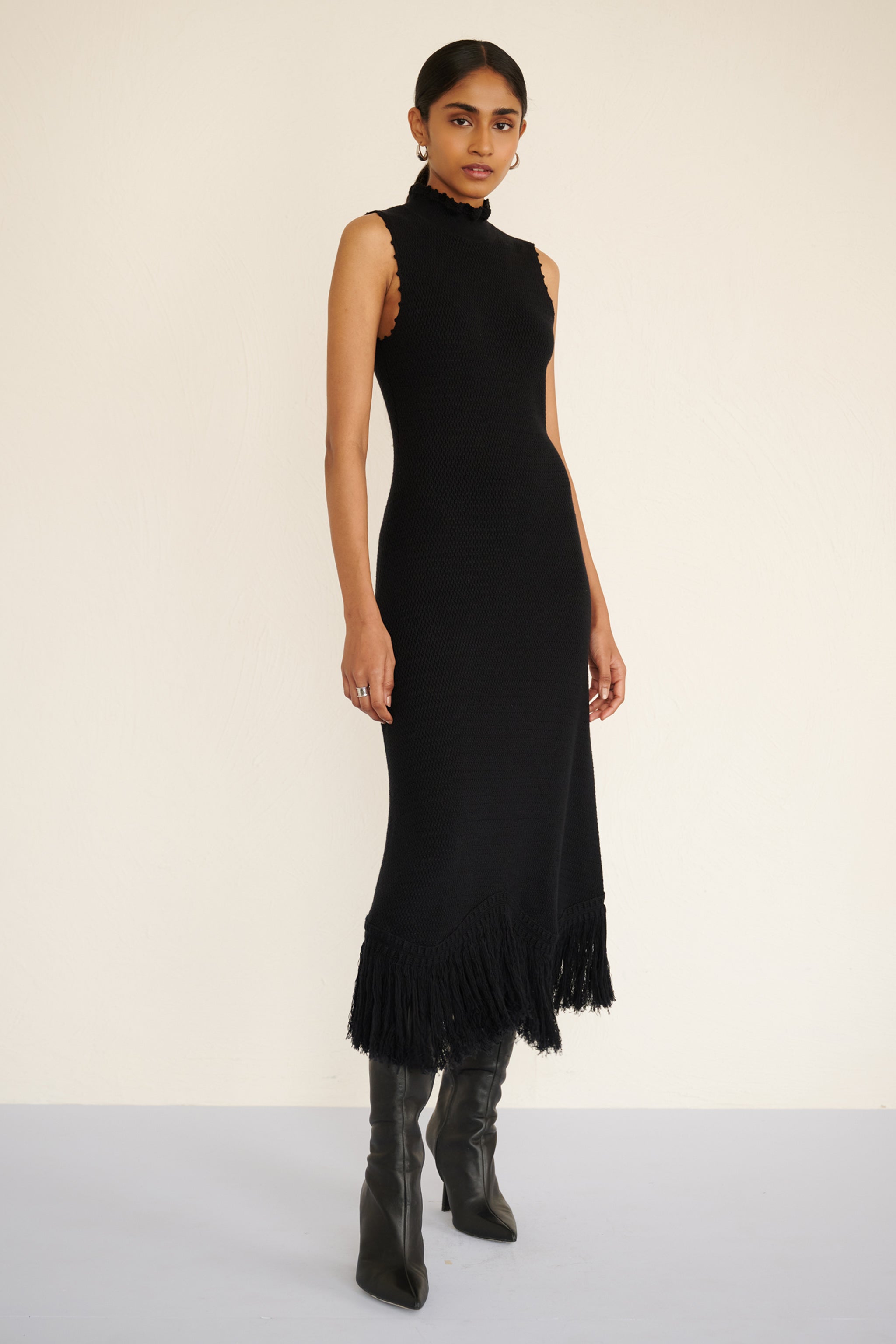 Front view of woman wearing a sleeveless cotton midi dress with a high neckline, hand-crocheted trim, and fringed asymmetrical hem.