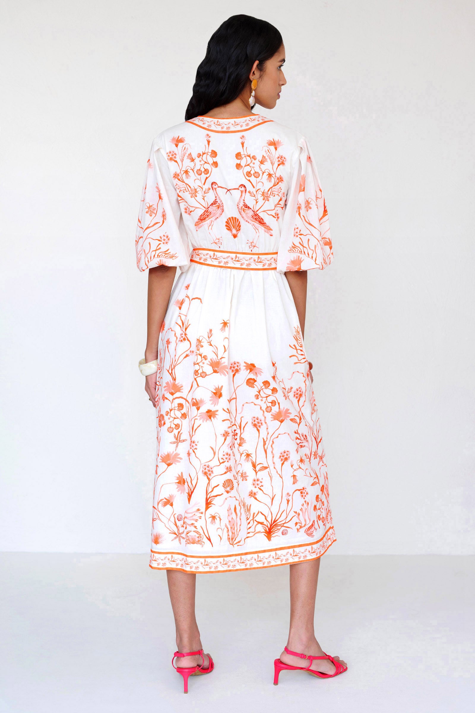 Back view of a woman standing wearing the Annabelle shirtdress in Tidepool print with hand in pocket. It features a V-neck, contrast trim & fabric tie waist.