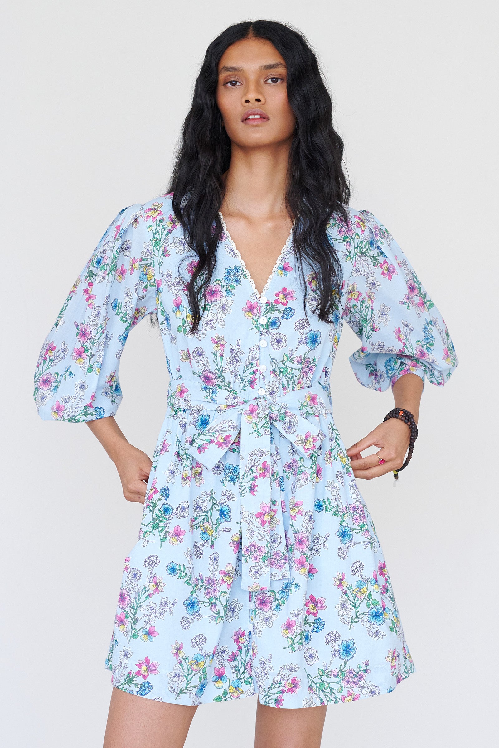 Front view close up of a woman standing wearing the Anne mini dress in Burdock Imperial print. It features long sleeves, lace-trimmed neck and cuffs, fabric belt, and side-seam pockets.