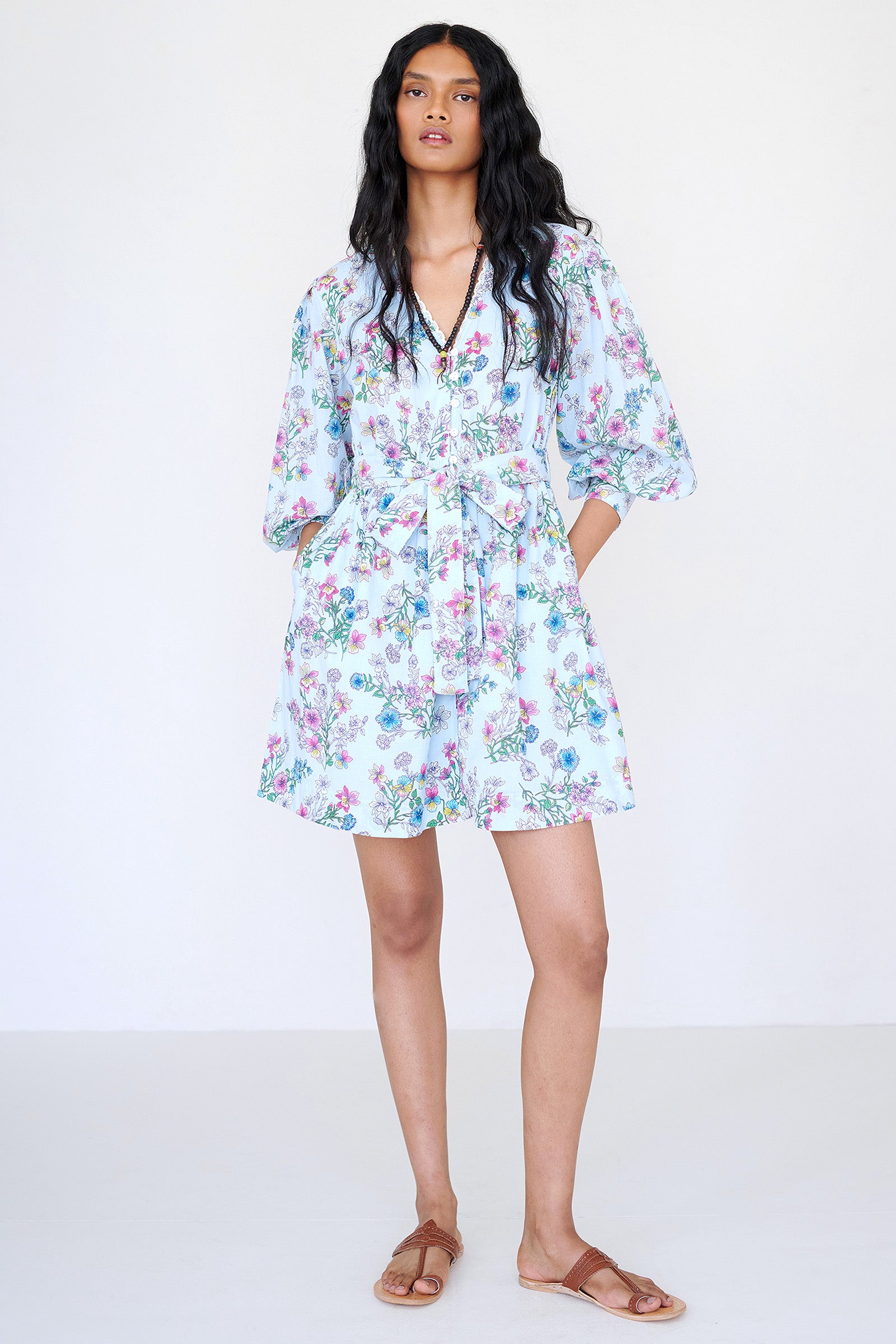 Front view of a woman standing wearing the Anne mini dress in Burdock Imperial print. It features long sleeves, lace-trimmed neck and cuffs, fabric belt, and side-seam pockets.