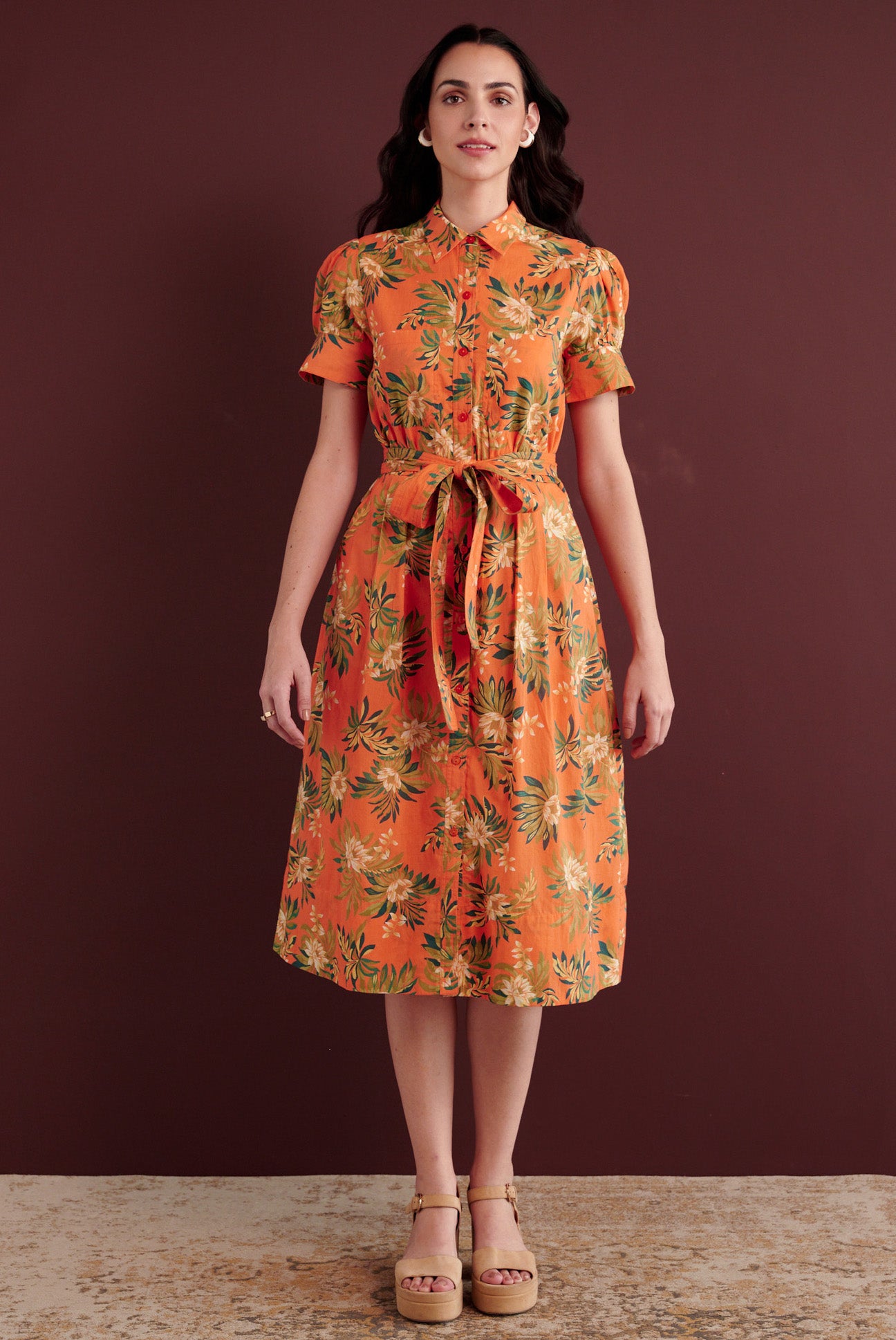 Front view of woman standing. She is wearing the Barbara day dress in Artichoke Flower print. It has gathered sleeves, chest pockets, fabric belt, button details, and a subtly structured yet romantic silhouette.