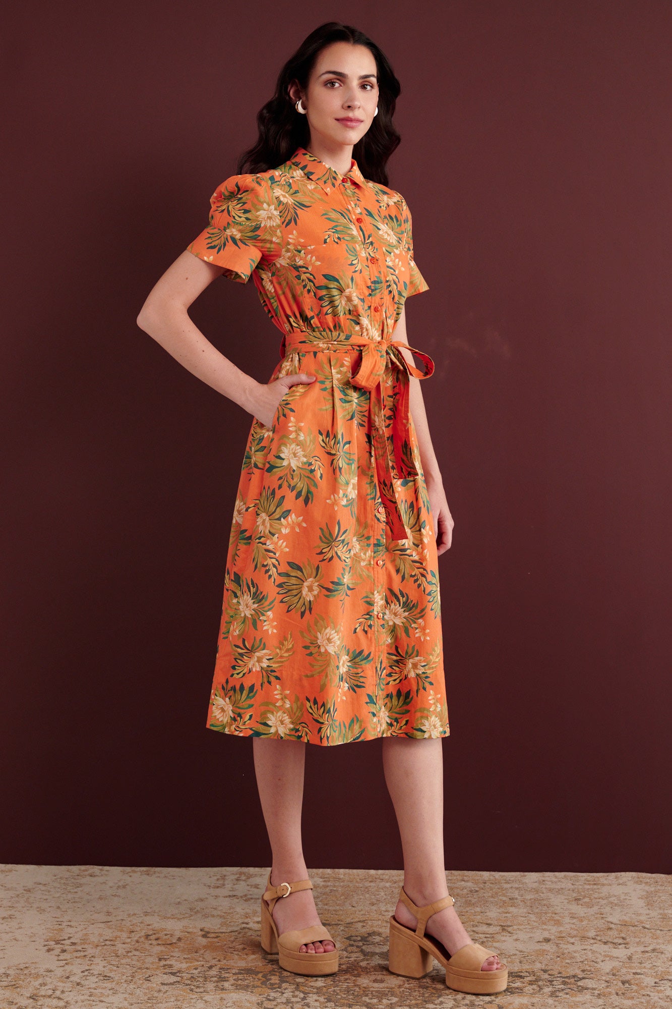Side view of woman standing. She is wearing the Barbara day dress in Artichoke Flower print. It has gathered sleeves, chest pockets, fabric belt, button details, and a subtly structured yet romantic silhouette.