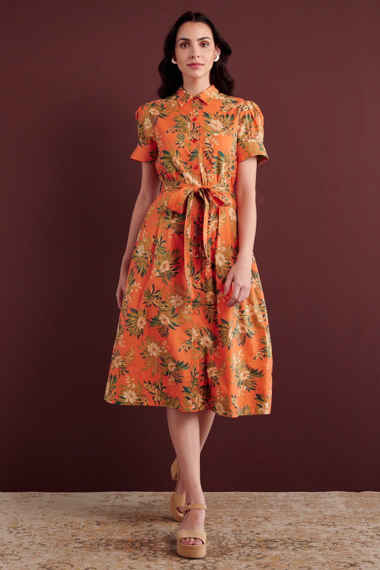 Front view of woman walking. She is wearing the Barbara day dress in Artichoke Flower print. It has gathered sleeves, chest pockets, fabric belt, button details, and a subtly structured yet romantic silhouette.