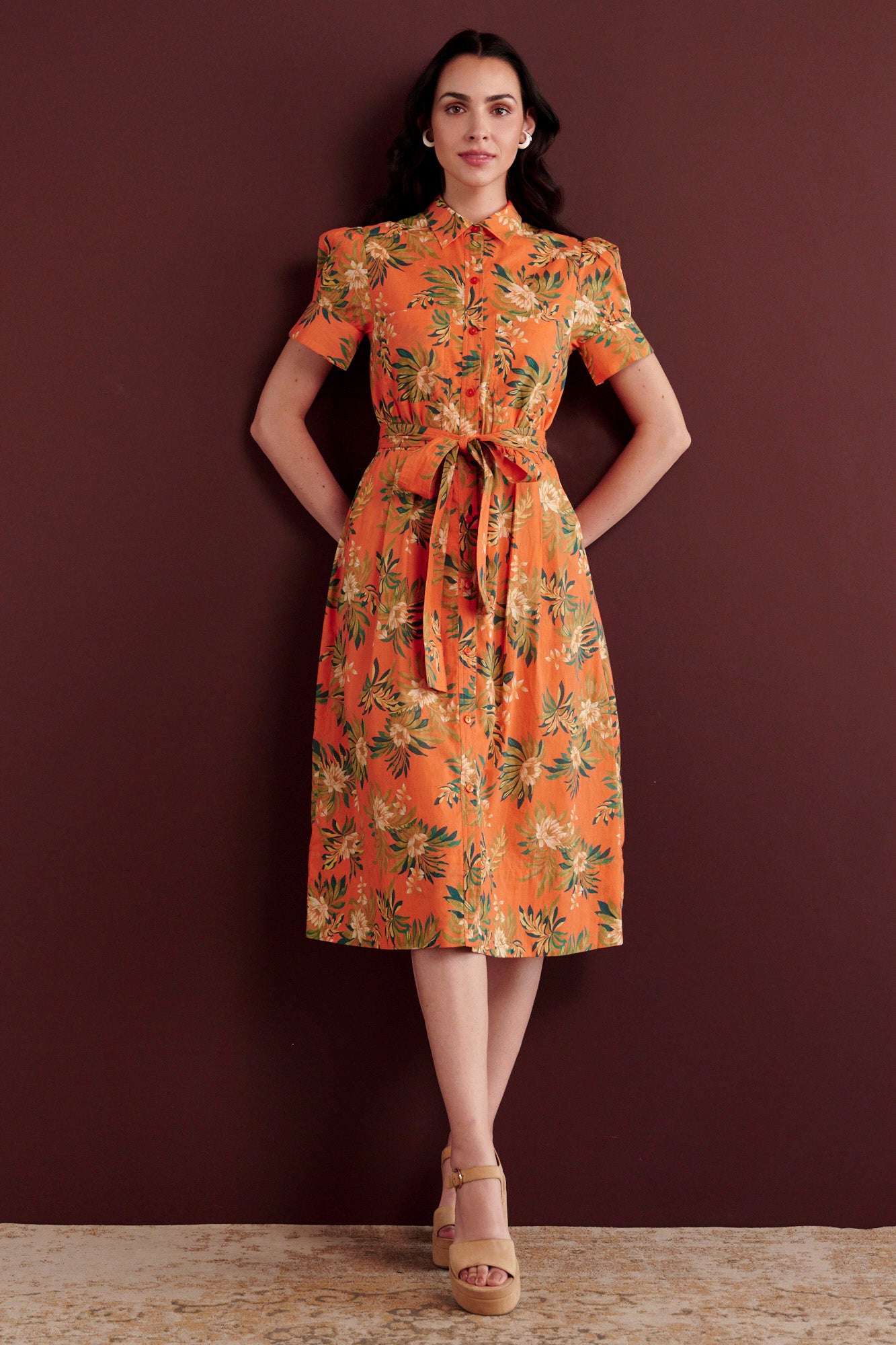 Front view of woman standing. She is wearing the Barbara day dress in Artichoke Flower print. It has gathered sleeves, chest pockets, fabric belt, button details, and a subtly structured yet romantic silhouette.