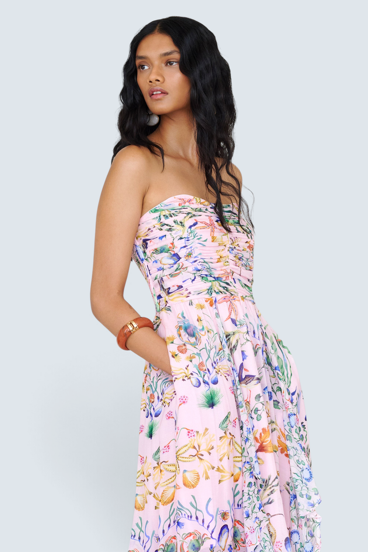 Side view close up of a woman standing wearing the Bella dress in Tidepool print, featuring a full-length cascading skirt with contrast frill, ruched bodice, smocked back, side-seam pockets, and drapey viscose voile.