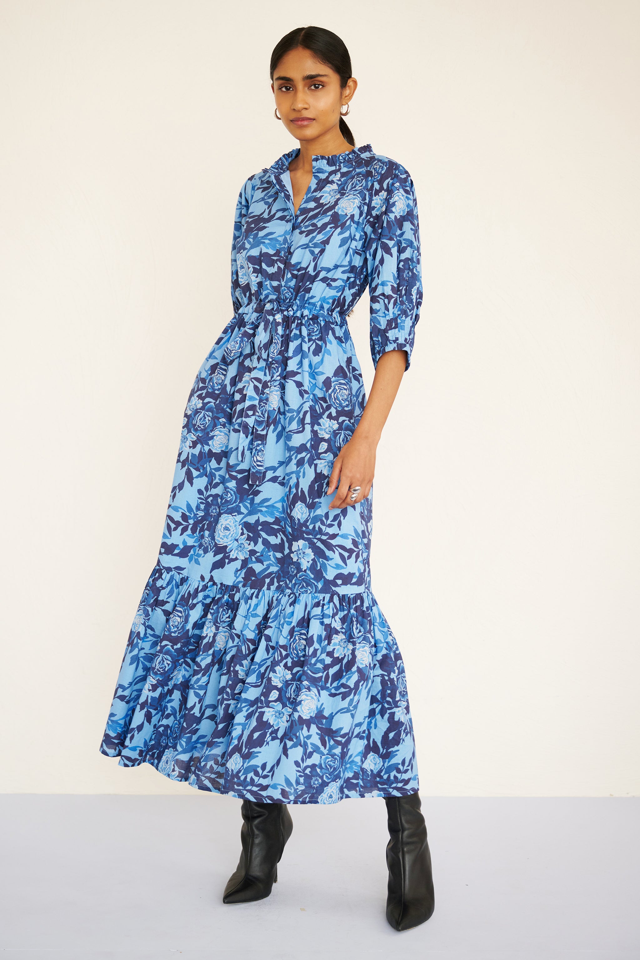 Front view of woman wearing a floral midi dress with raglan sleeves, gathered skirt, tie belt at the waist, and a soft watercolor rose print in tones of blue.