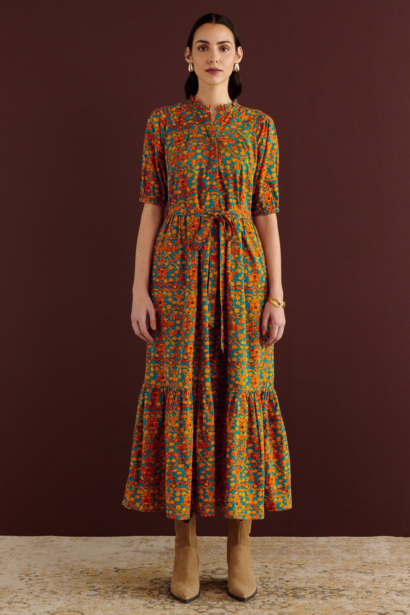 Front view of woman standing. She is wearing the Betty dress in Ottoman print. It has nipped waist, full gathered skirt, tucked raglan sleeves, cotton voile fabric, fabric tie belt, fully lined construction, and side-seam pockets.