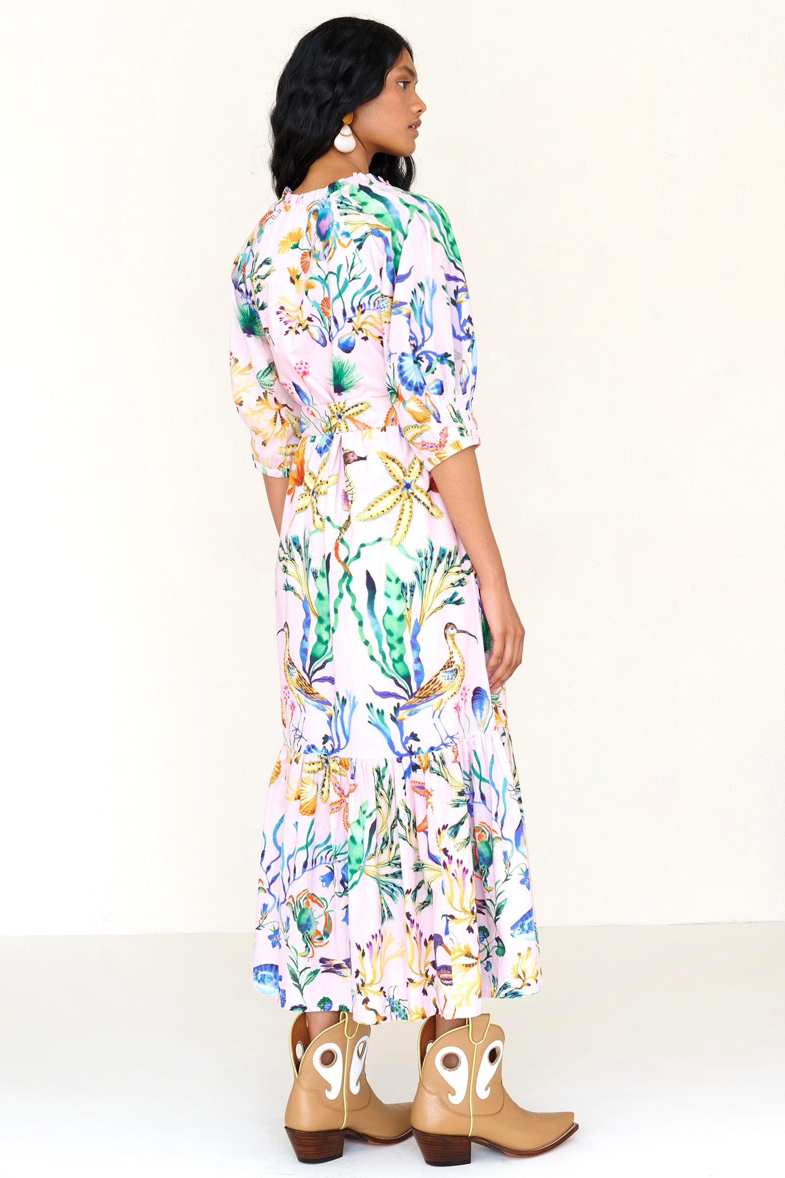 Back view of a woman standing. She is wearing the Betty dress in Tidepool print. It features a nipped waist, voluminous gathered skirt, tucked raglan sleeves, fabric tie belt & pockets.