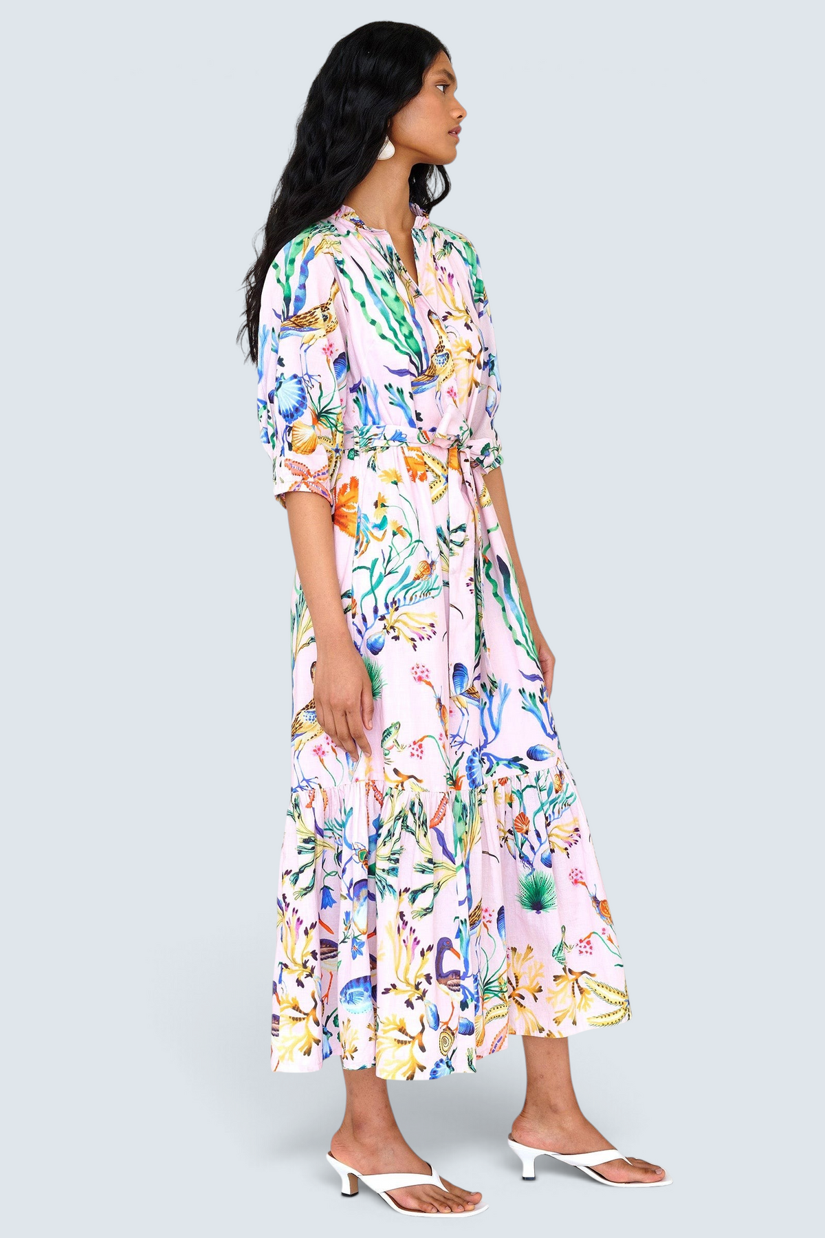 Side view of a woman standing. She is wearing the Betty dress in Tidepool print. It features a nipped waist, voluminous gathered skirt, tucked raglan sleeves, fabric tie belt & pockets.