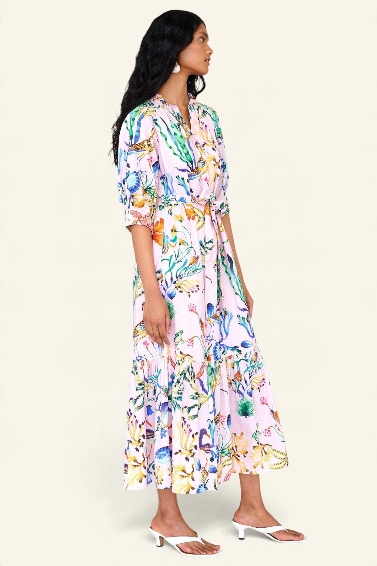 Side view of a woman standing. She is wearing the Betty dress in Tidepool print. It features a nipped waist, voluminous gathered skirt, tucked raglan sleeves, fabric tie belt & pockets.