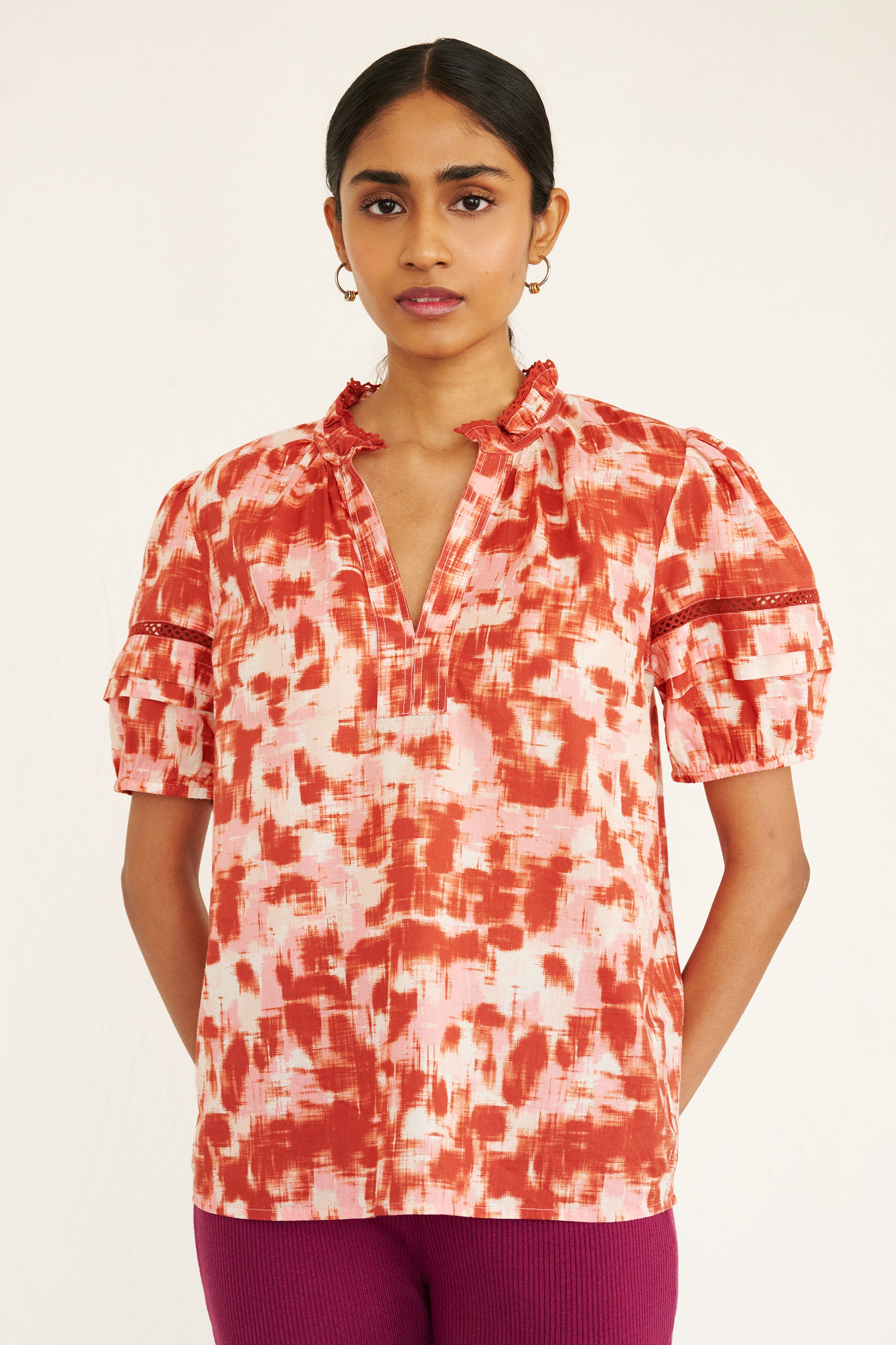 Front view of woman wearing a cotton top with an ikat-inspired print, lace sleeve insets, a split neckline, and pleated sleeves.