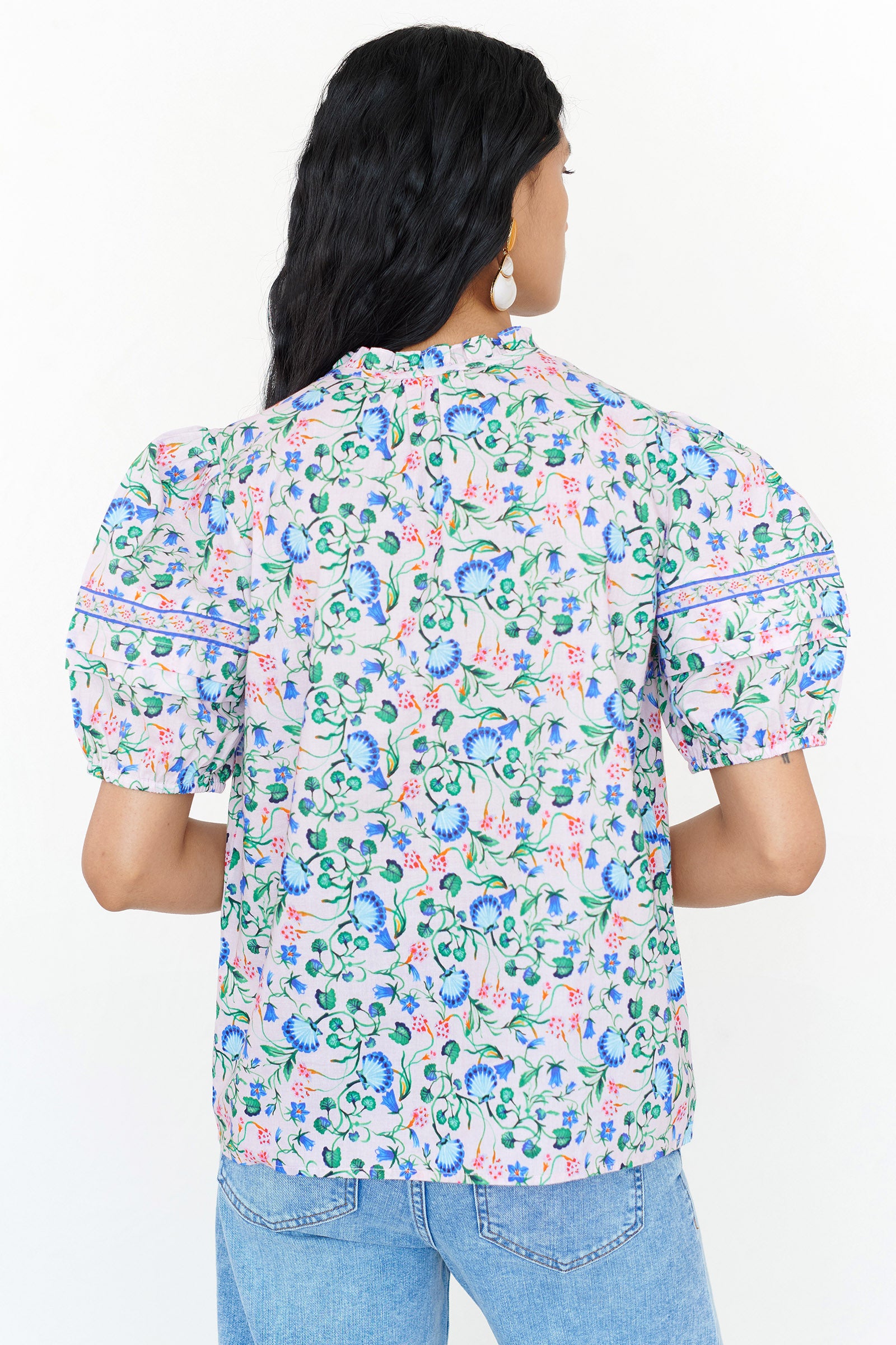 Back view of a woman standing. She is wearing the Bronte top in Clam Garland print, featuring a front opening, delicate neckline detailing, contrast trim, and softly pleated sleeves styled with denim.