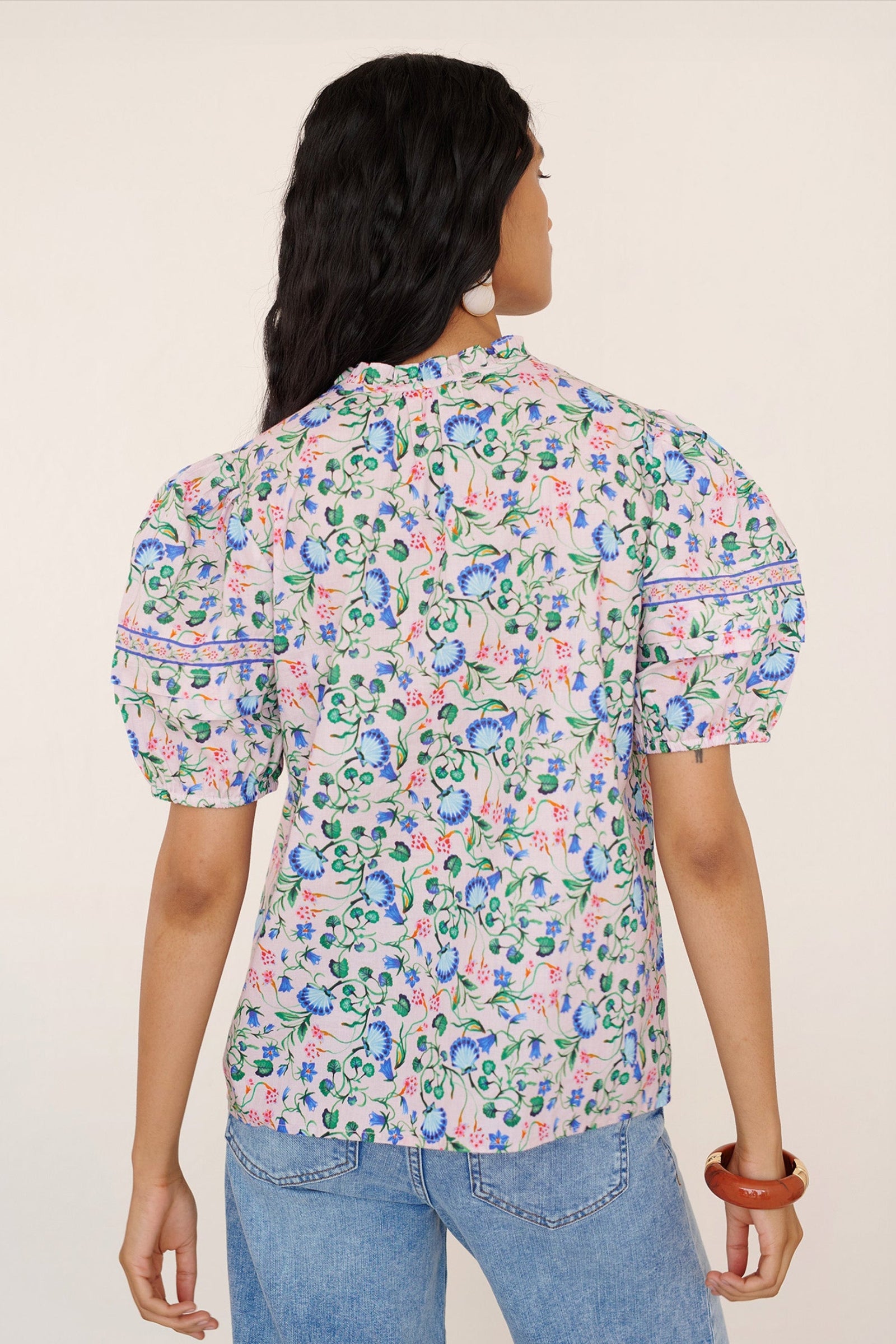 Back view of a woman standing. She is wearing the Bronte pullover top in Clam Garland print paired with jeans. It features a front opening, contrast trim at the neck, and pleated sleeves.