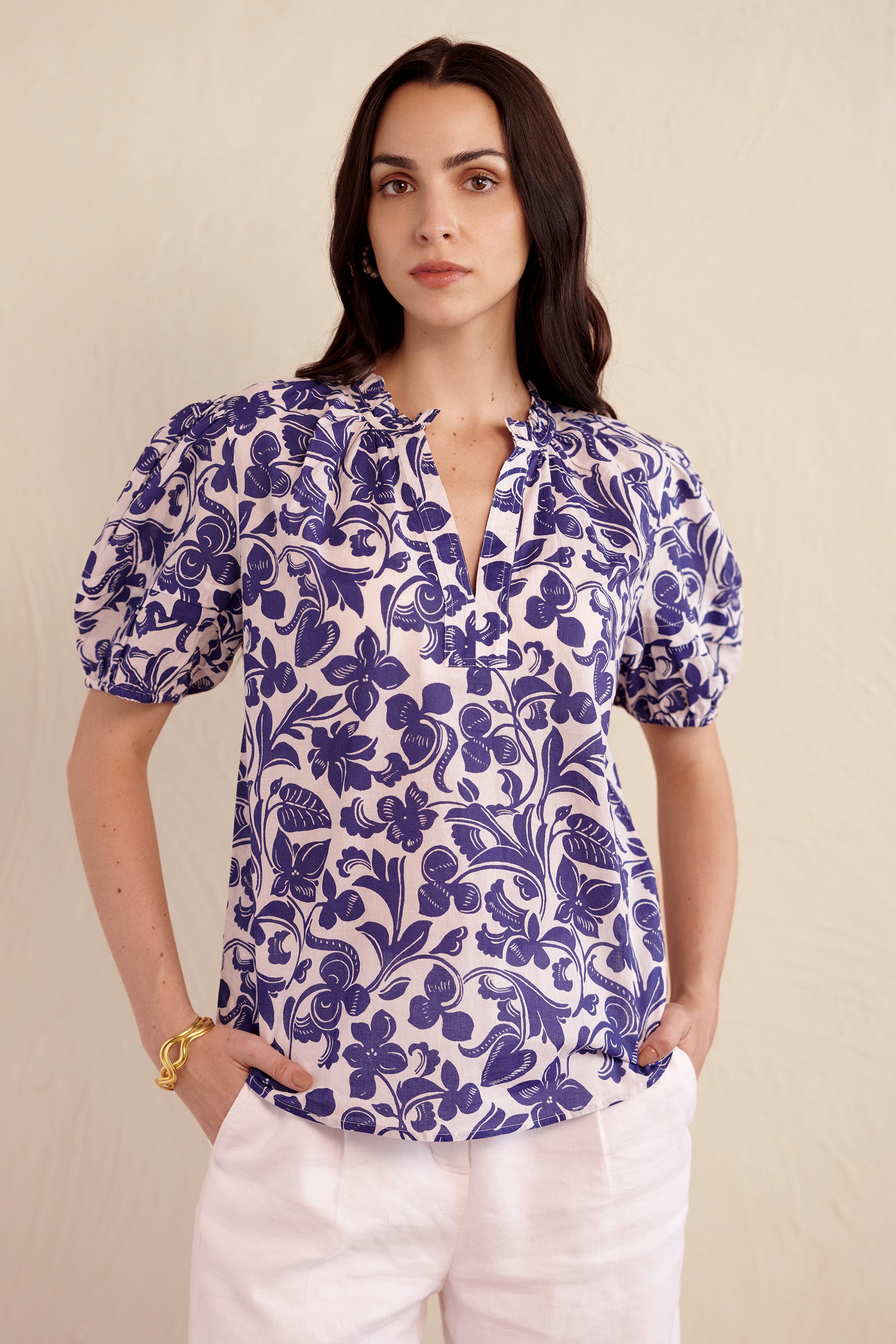 Front view of woman wearing the Bronte top in blue and white Gaia floral print, featuring a front opening, pleated sleeves, and delicate neckline detailing.