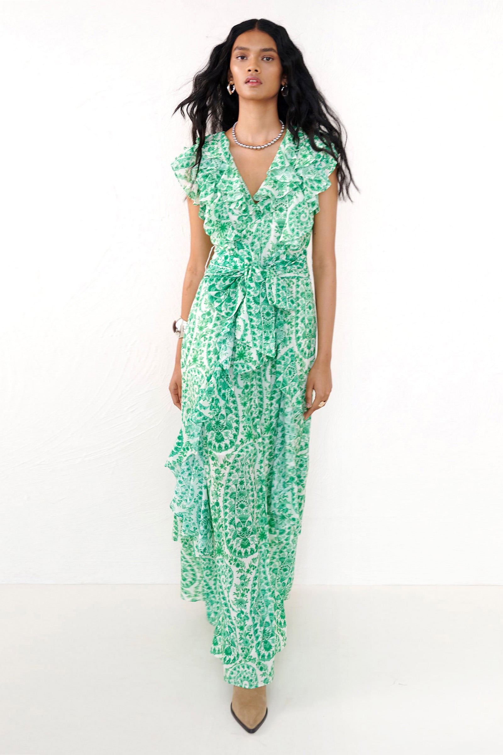 Front view of a woman walking forward. She is wearing the Beatrice dress in Paisley print, featuring a full-length tiered skirt, ruffled bodice, fabric tie belt, dramatic tie-back neckline, and lustrous cotton silk.