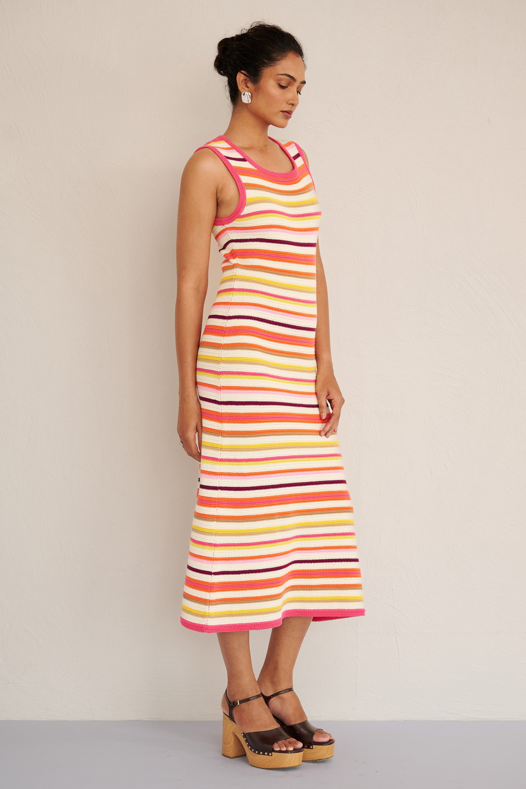 Side view of woman wearing the Calla dress in bright citrus stripes, featuring a sleeveless, body-skimming silhouette with ribbed trims, made from organic cotton.