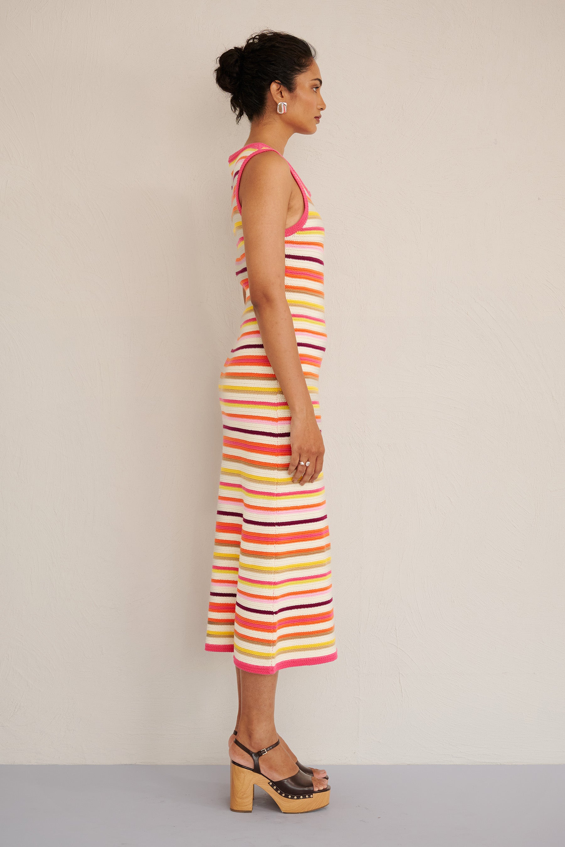 Side view of woman wearing the Calla dress in bright citrus stripes, featuring a sleeveless, body-skimming silhouette with ribbed trims, made from organic cotton.