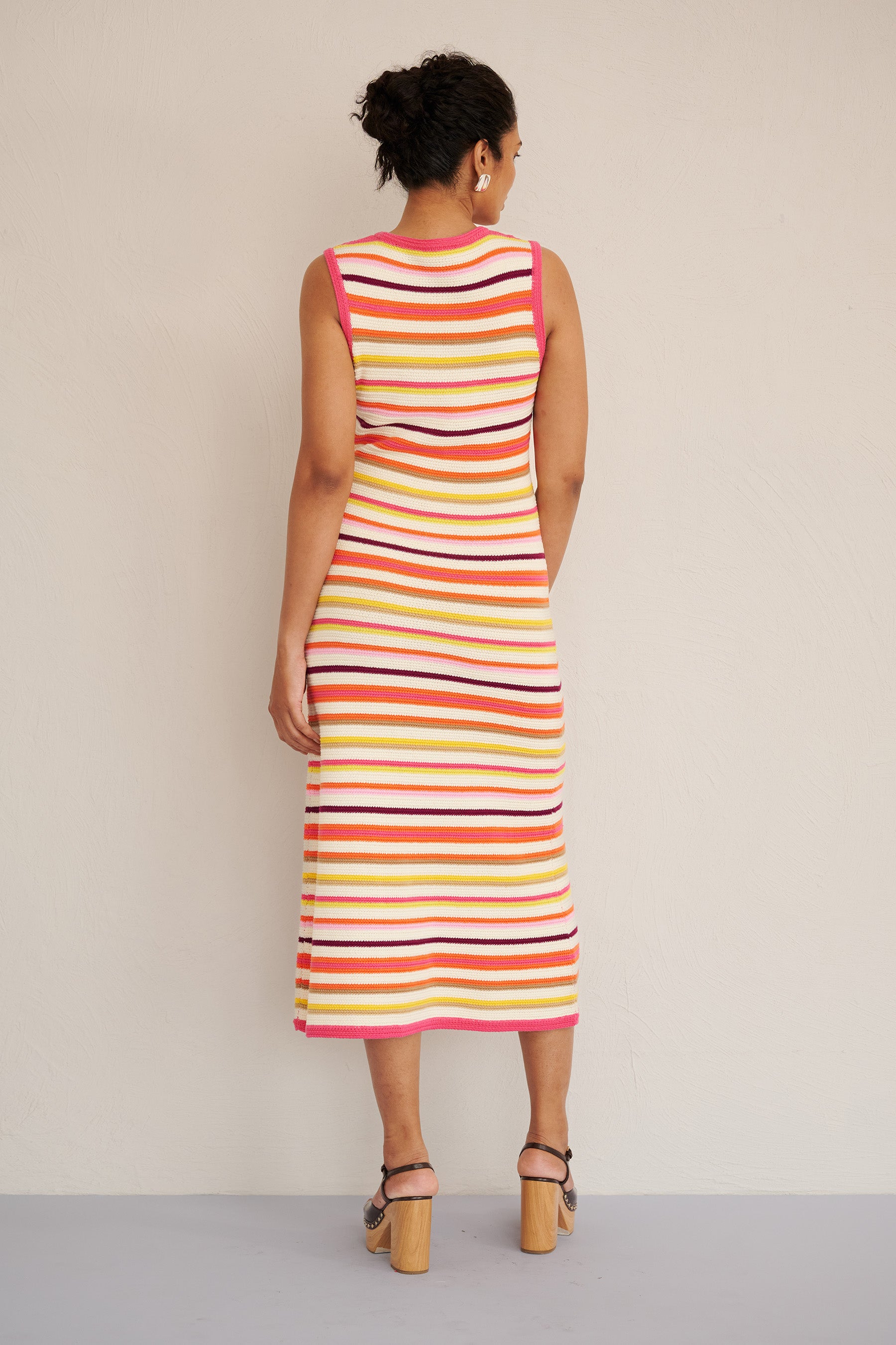 Back view of woman wearing the Calla dress in bright citrus stripes, featuring a sleeveless, body-skimming silhouette with ribbed trims, made from organic cotton.