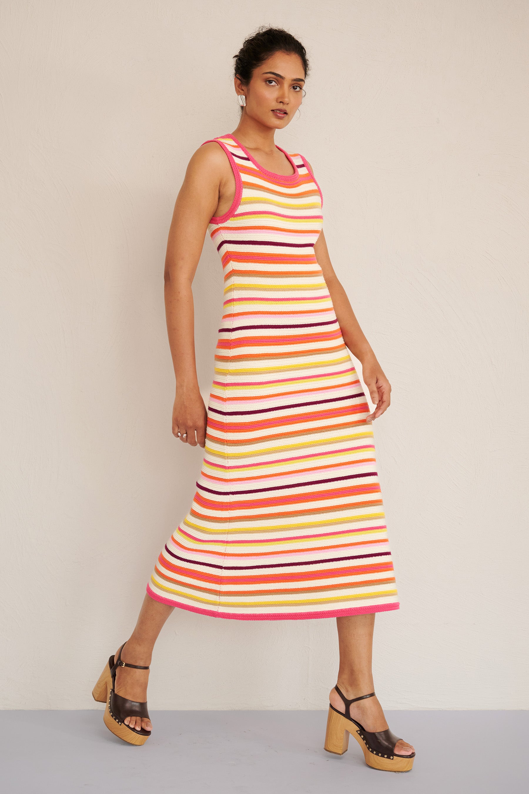 Side view of woman wearing the Calla dress in bright citrus stripes, featuring a sleeveless, body-skimming silhouette with ribbed trims, made from organic cotton.