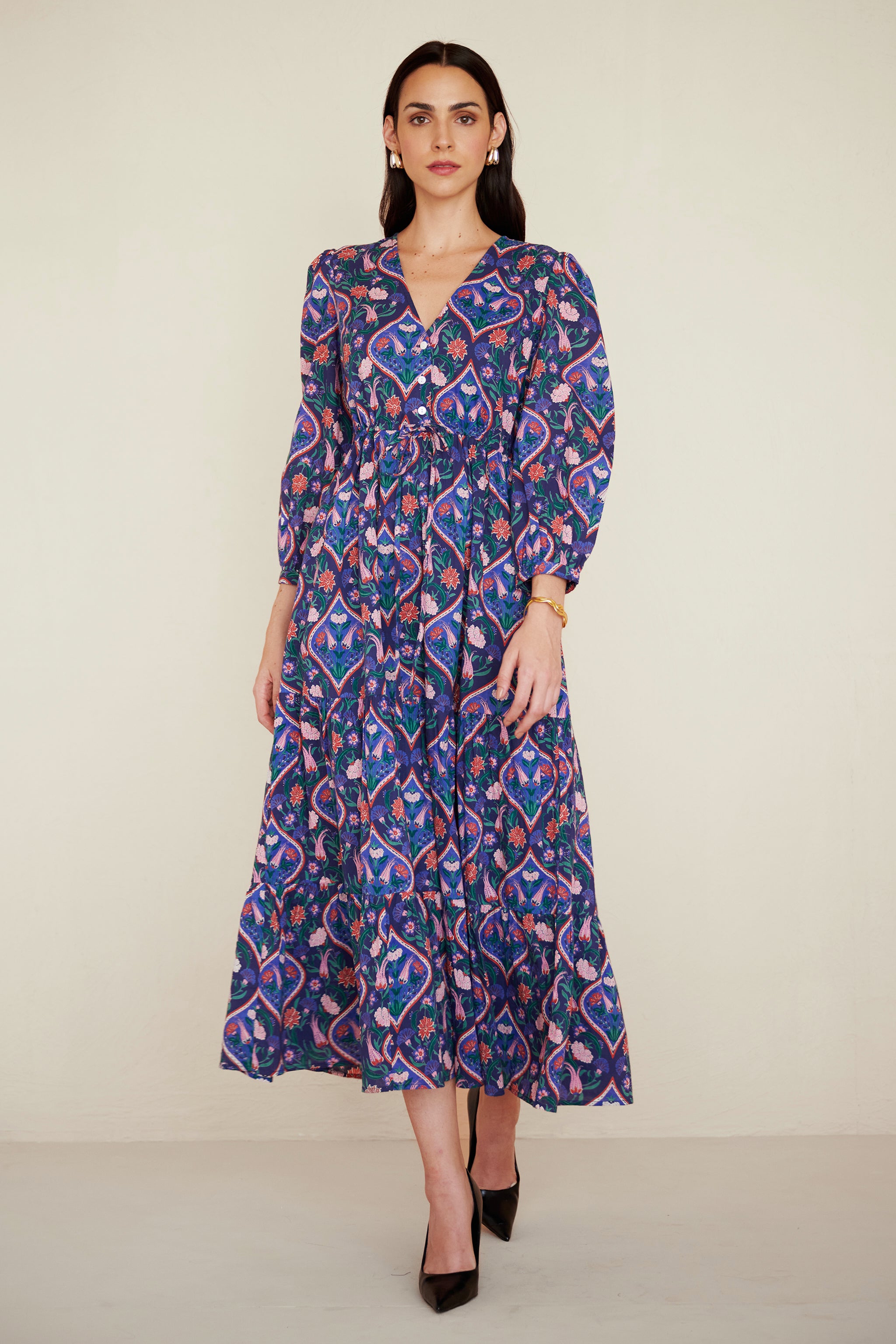 Front view of woman wearing a cotton midi dress with puff sleeves and a gathered drawstring skirt, featuring a floral tile print and side pockets.