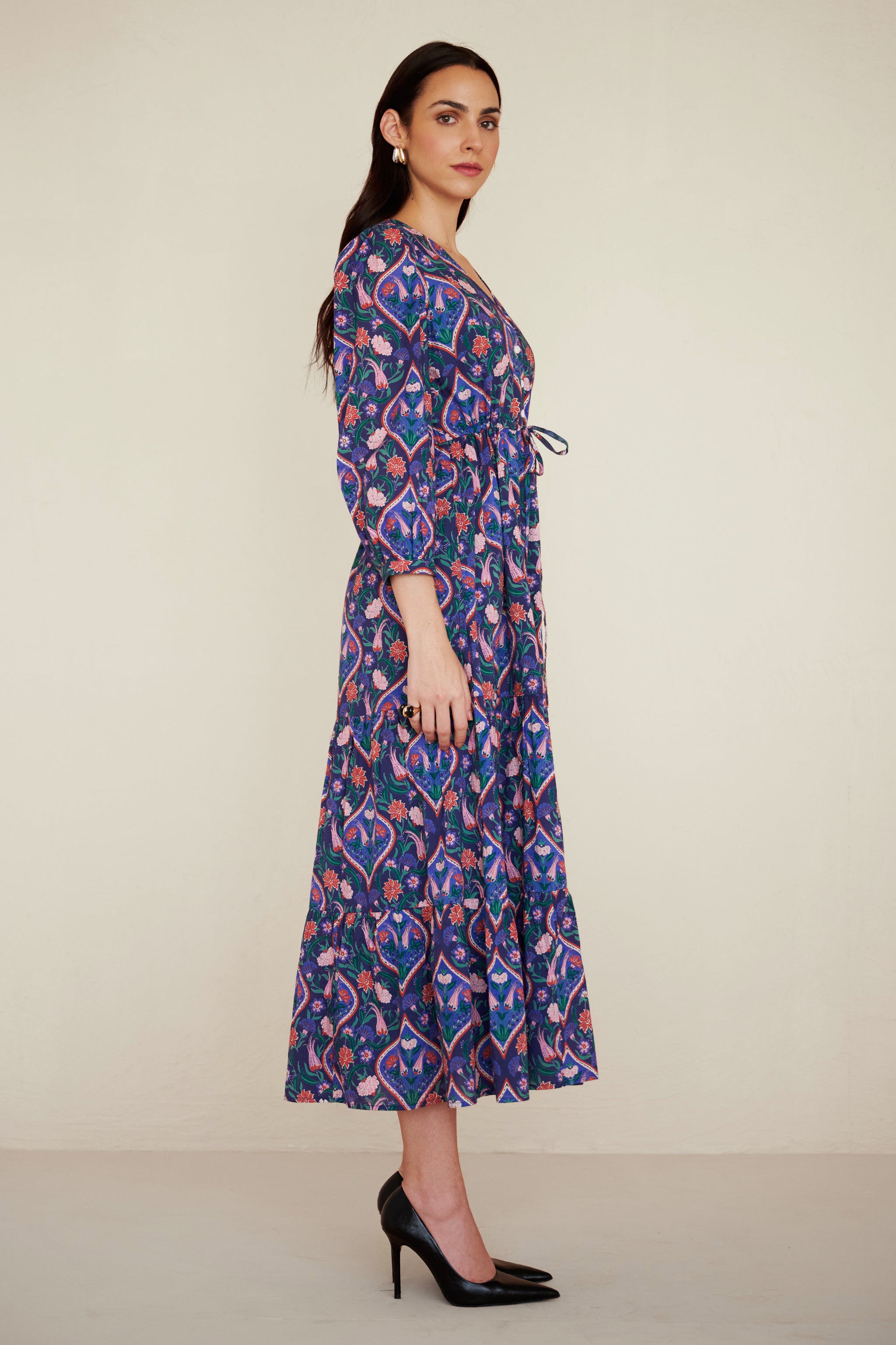 Side view of woman wearing a cotton midi dress with puff sleeves and a gathered drawstring skirt, featuring a floral tile print and side pockets.