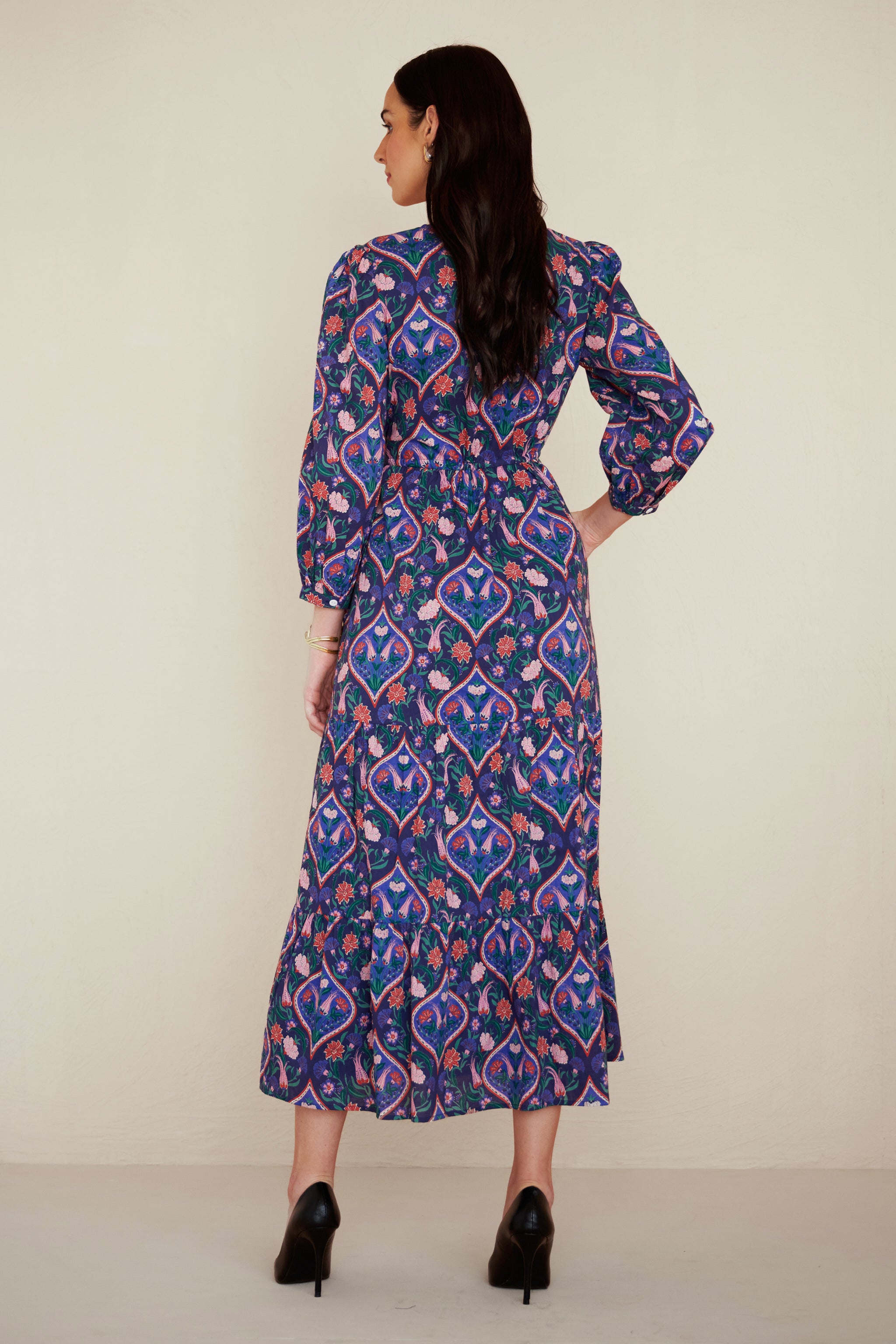 Back view of woman wearing a cotton midi dress with puff sleeves and a gathered drawstring skirt, featuring a floral tile print and side pockets.