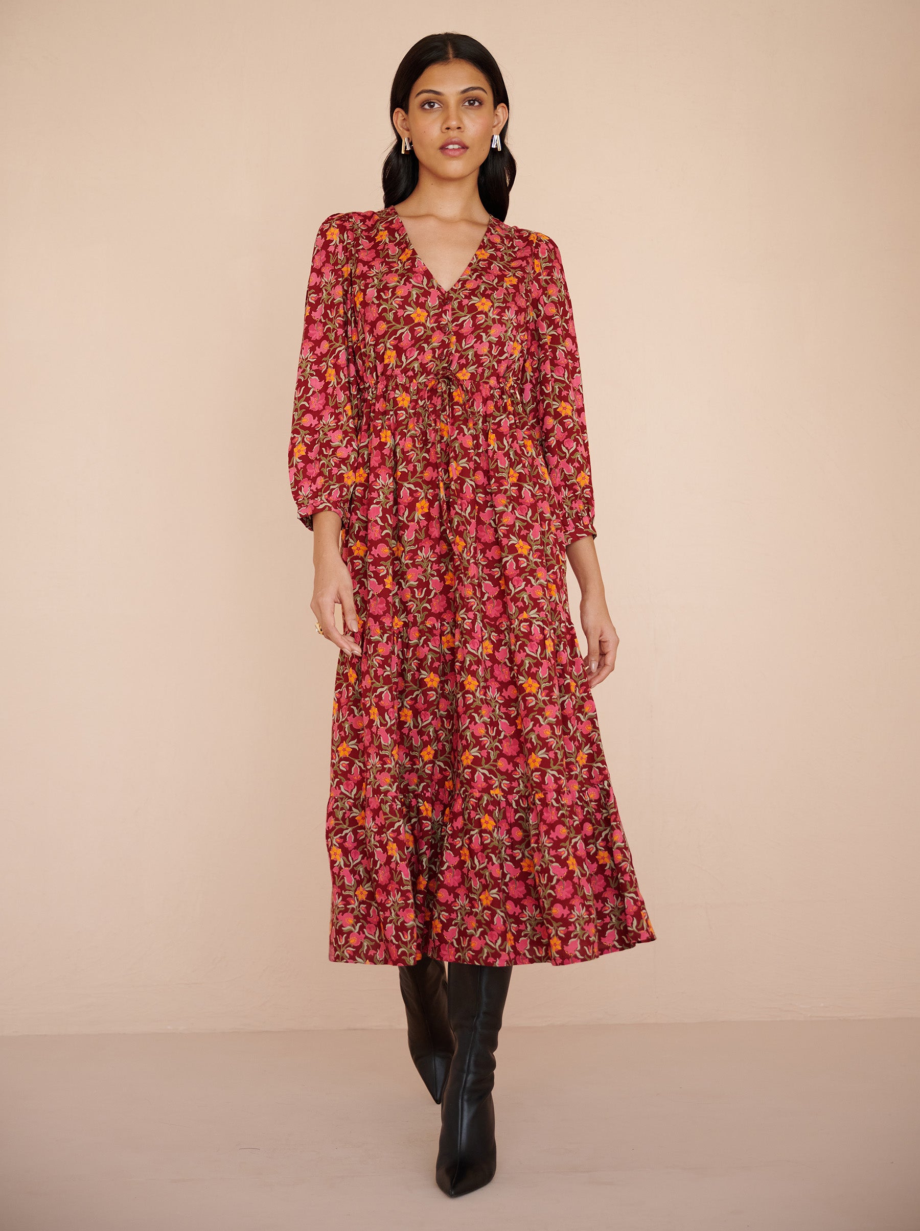 Front view of a model walking. She is wearing the Castor dress in eco-friendly viscose. It is featuring soft puff sleeves, a gathered drawstring skirt to the shin, and the Pomegranate Vine print in Azalea color. The dress is fully lined with side-seam pockets.