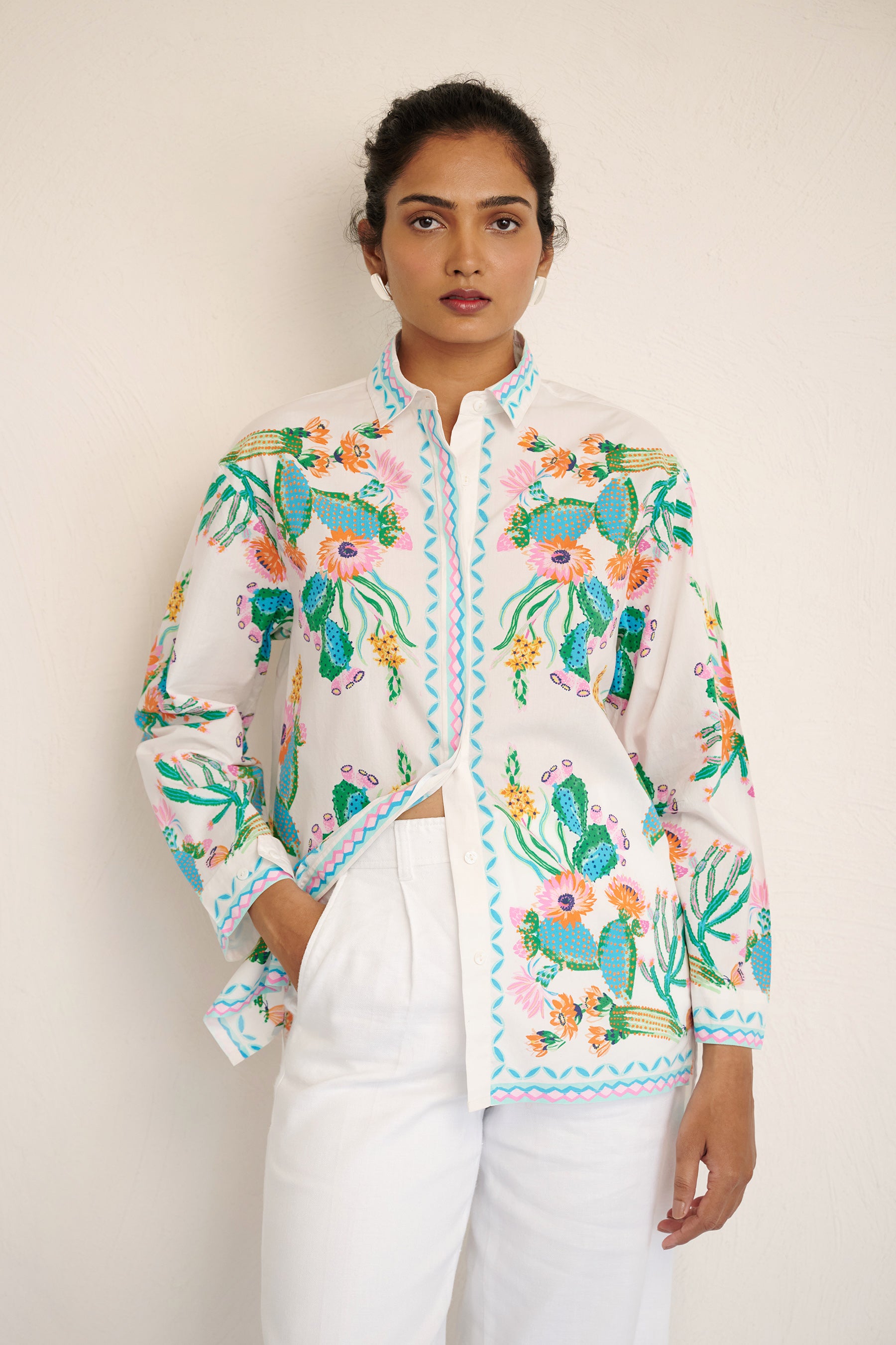 Front view of woman wearing the Charlotte shirt in Calypso Cacti print, featuring a button-up front, high-low hem, and a back box pleat, printed with cactus blossoms and geometric borders.