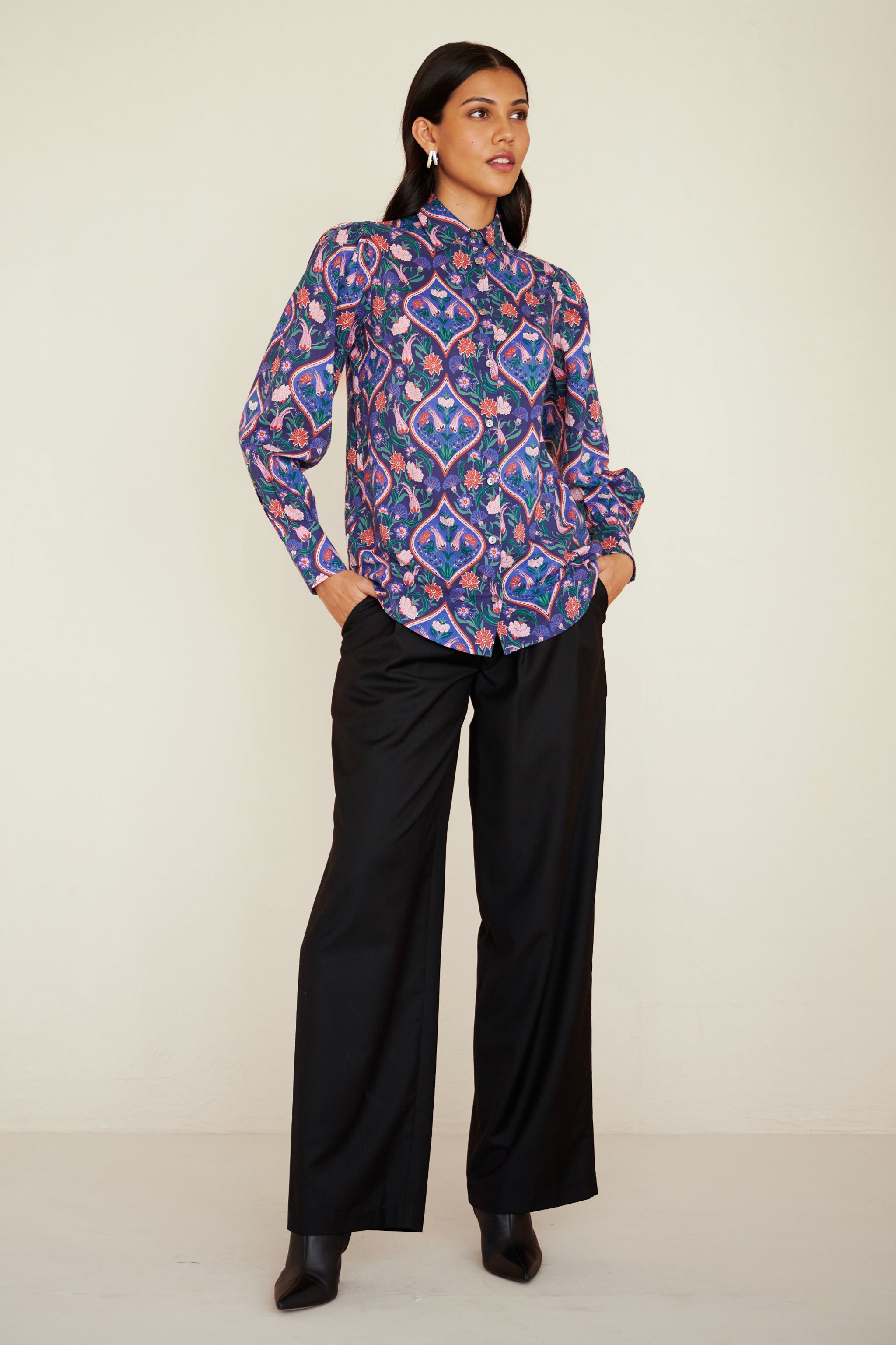 Front view of woman wearing a relaxed-fit button-down shirt with floral tile print, straight collar, and full sleeves with buttoned cuffs.