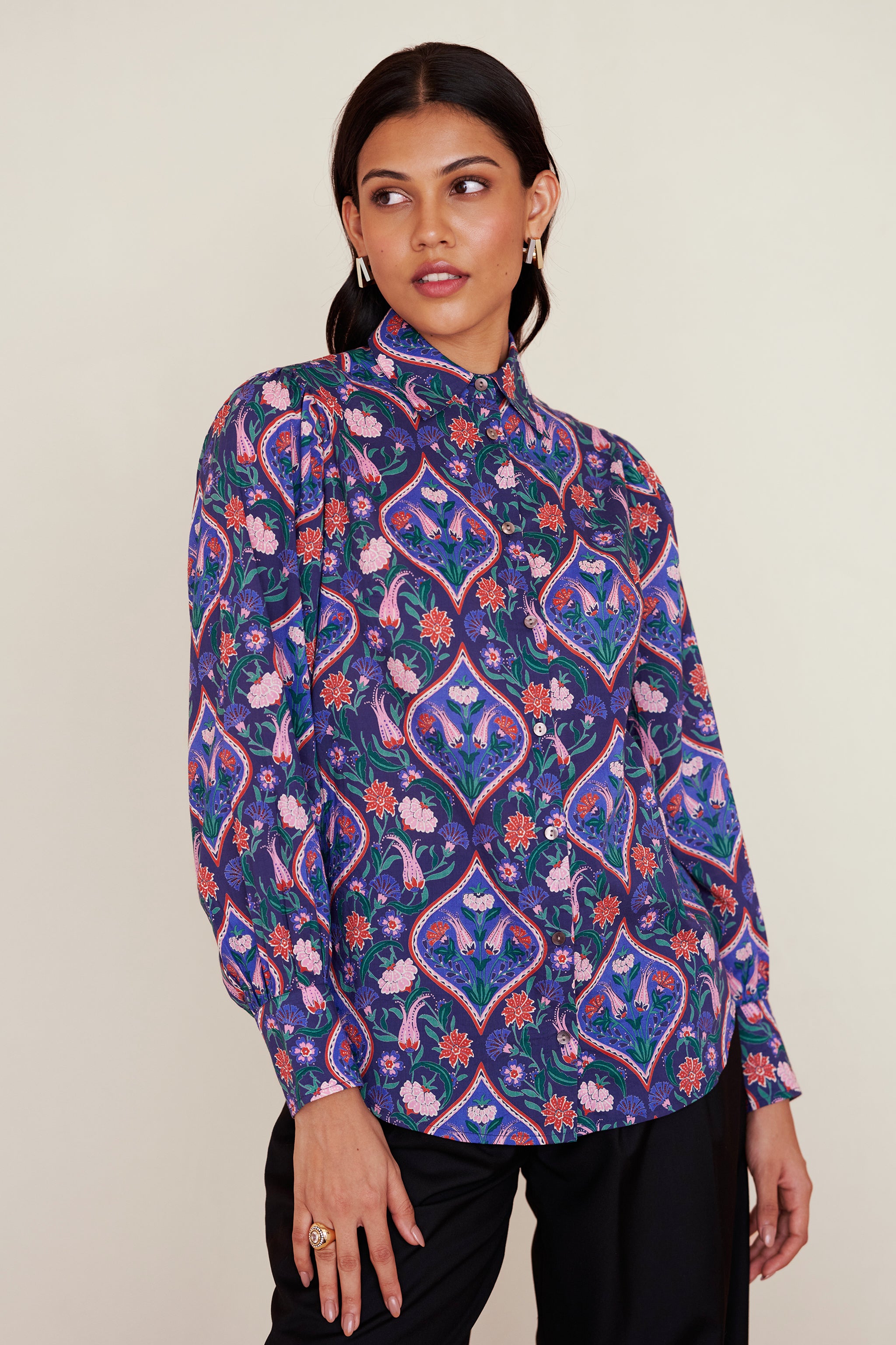 Front view of woman wearing a relaxed-fit button-down shirt with floral tile print, straight collar, and full sleeves with buttoned cuffs.
