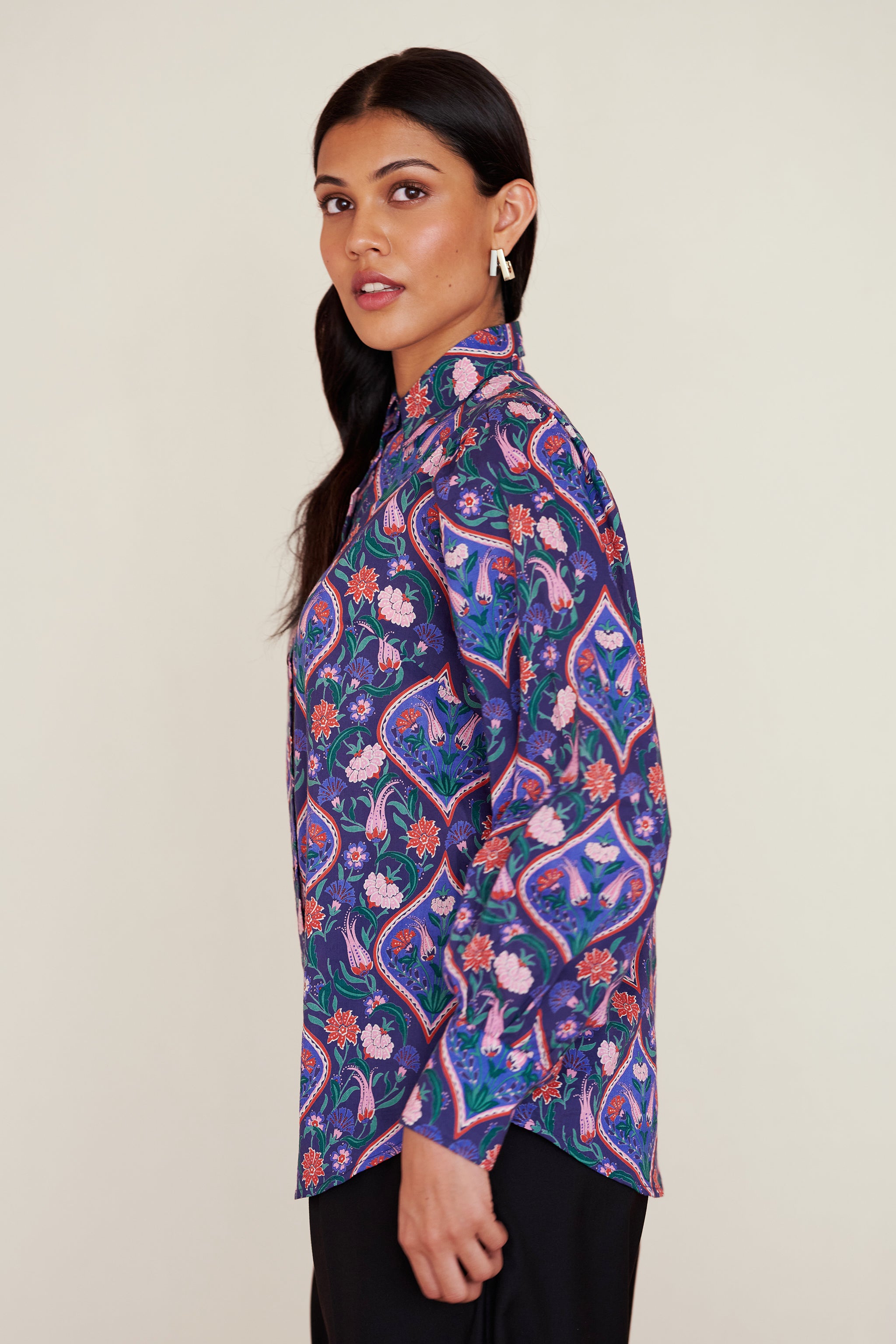 Side view of woman wearing a relaxed-fit button-down shirt with floral tile print, straight collar, and full sleeves with buttoned cuffs.