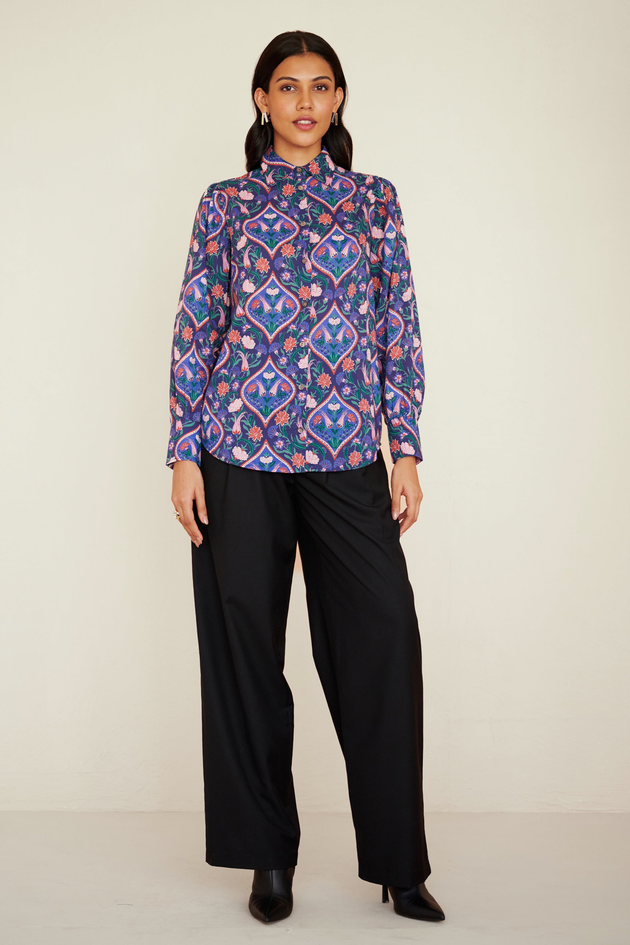 Front view of woman wearing a relaxed-fit button-down shirt with floral tile print, straight collar, and full sleeves with buttoned cuffs.