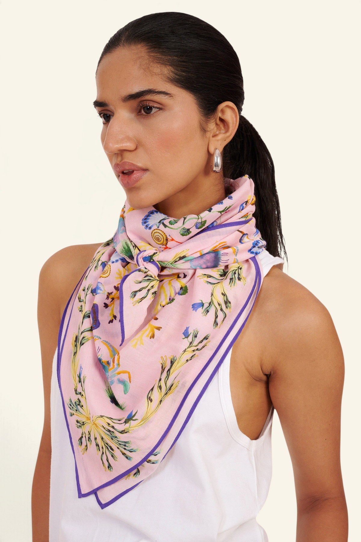 Front side-view close-up of woman standing, wearing the Carolina scarf around her neck in the Tidepool print featuring starfish, seahorse, and shell motifs.