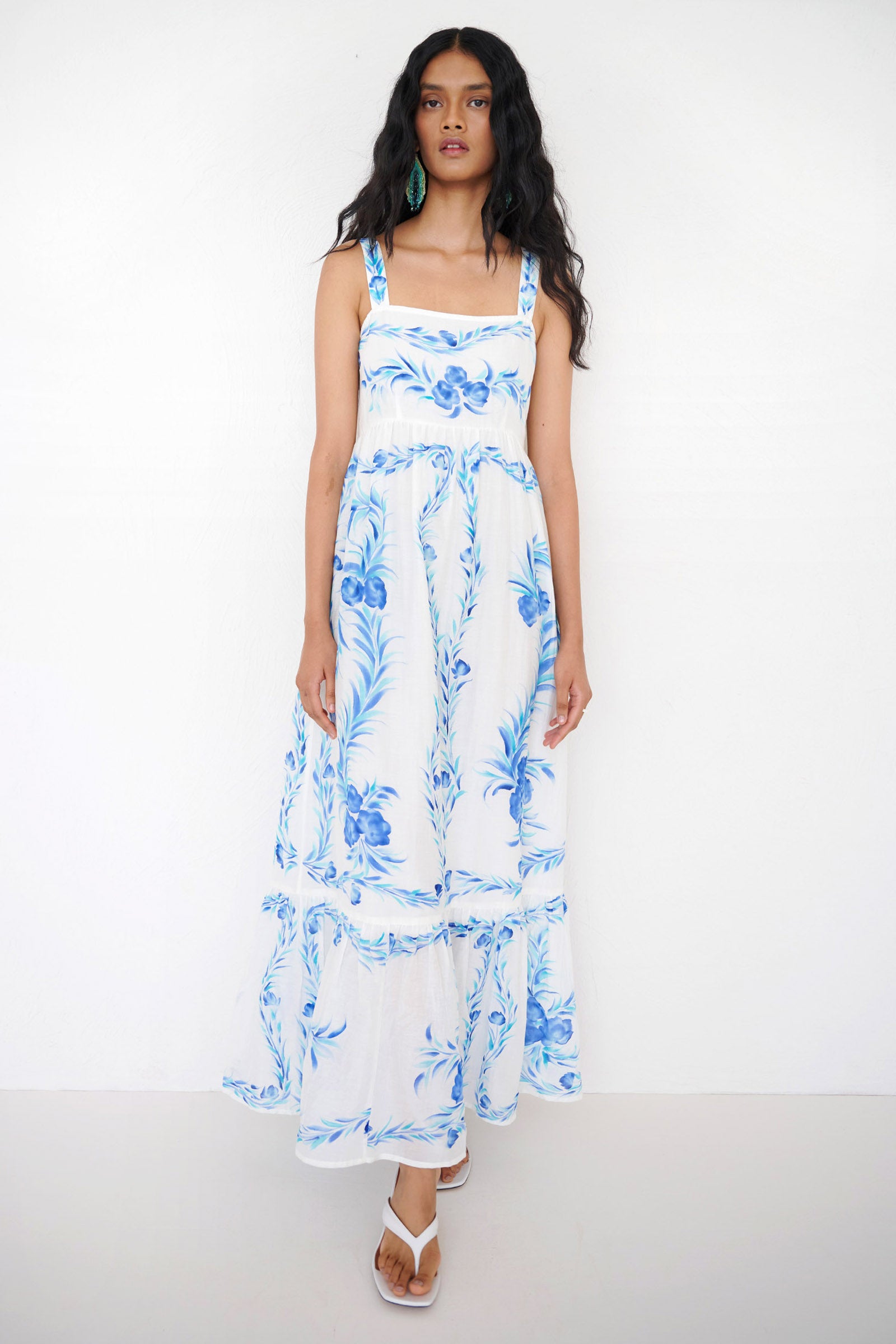 Front view of a woman walking wearing the Daniella dress, featuring hand-painted floral vignettes, ankle-grazing hem, straight neckline and side-seam pockets.