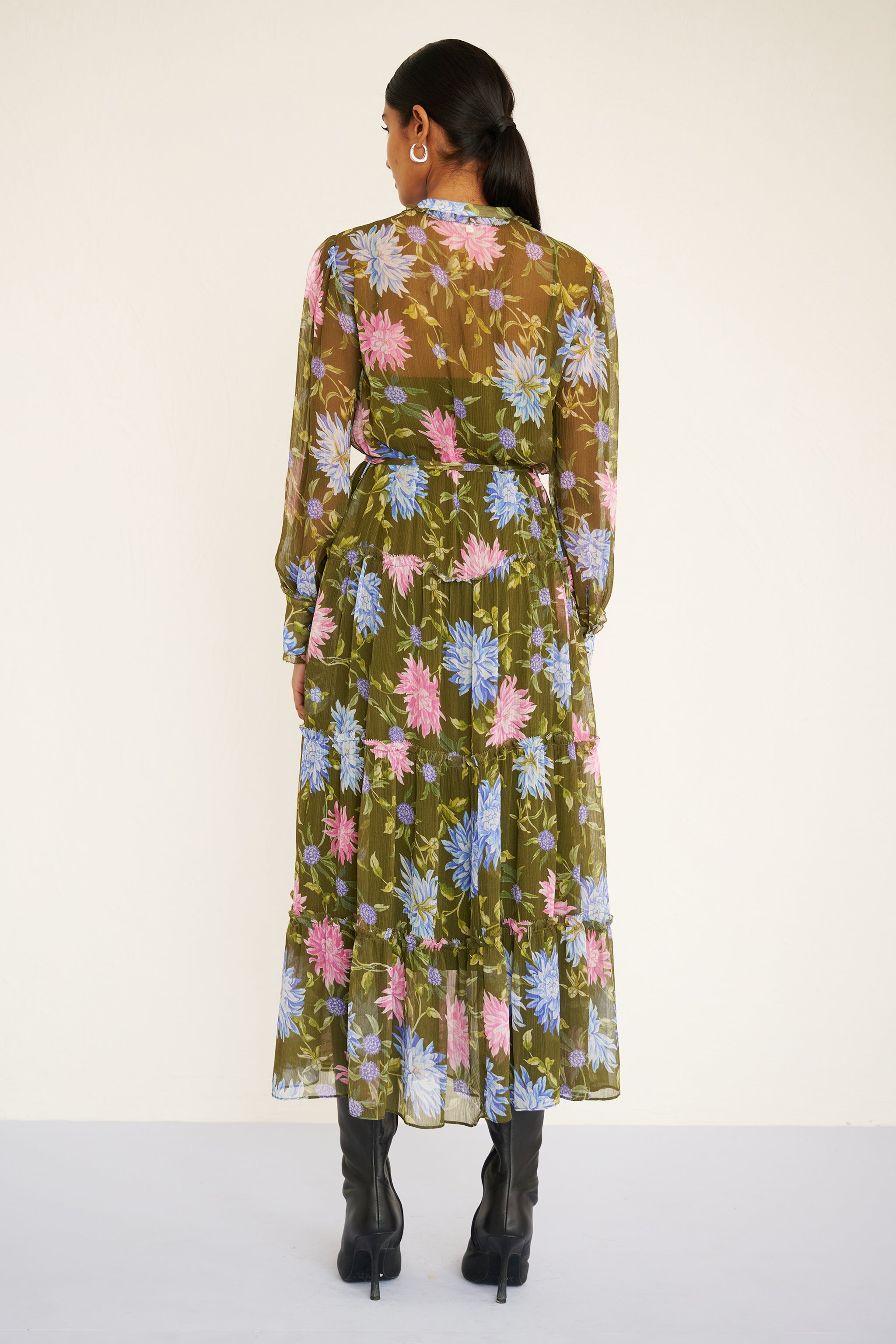 Back view of woman wearing a long-sleeve chiffon midi dress with sheer sleeves, ruffle details, fabric buttons, and a painterly floral print, styled with a detachable belt.