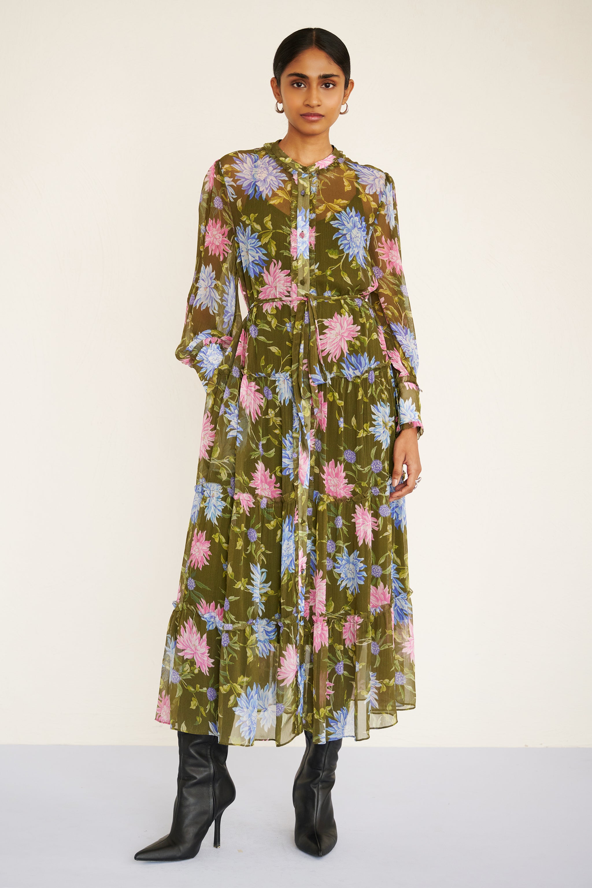 Front view of woman wearing a long-sleeve chiffon midi dress with sheer sleeves, ruffle details, fabric buttons, and a painterly floral print, styled with a detachable belt.