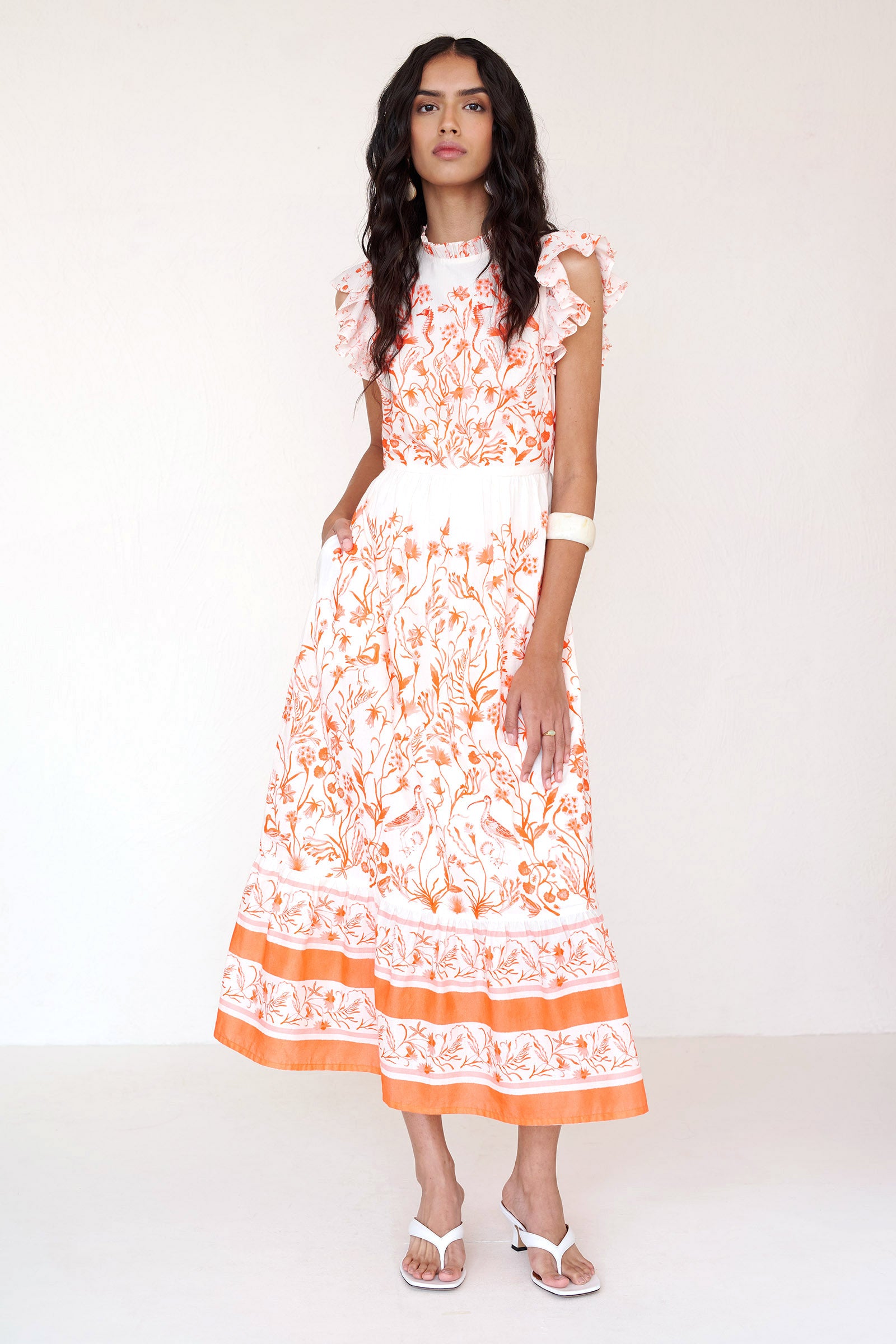 Front view of a woman standing wearing the Hannah dress in Tidepool print. It features ruffled neckline, tiered skirt, back keyhole with button closure & side-seam pockets.