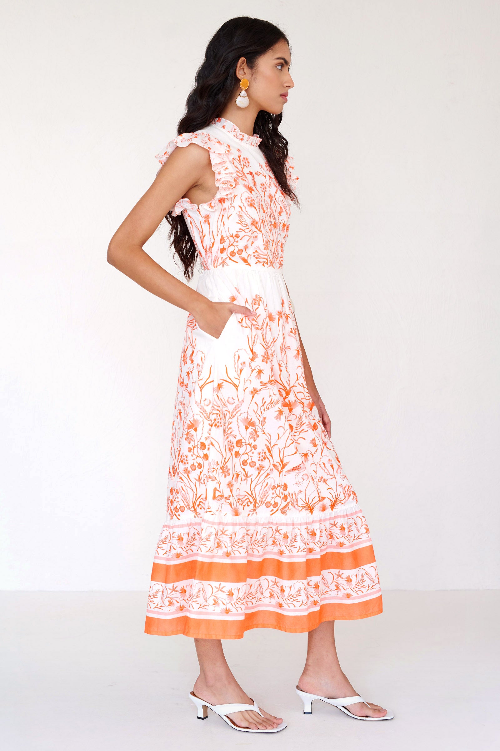 Side view of a woman standing wearing the Hannah dress in Tidepool print. It features ruffled neckline, tiered skirt, back keyhole with button closure & side-seam pockets.