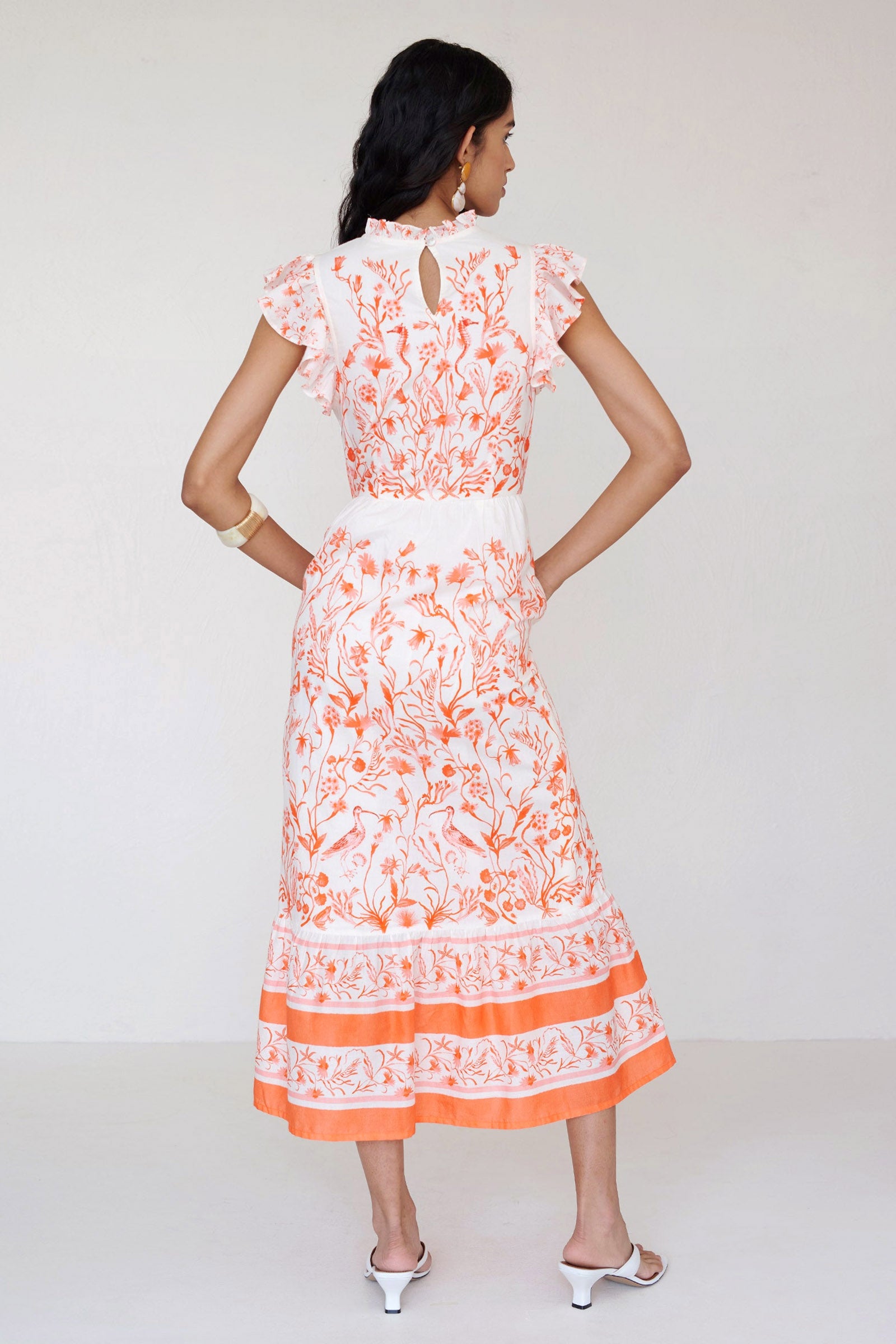 Back view of a woman standing wearing the Hannah dress in Tidepool print. It features ruffled neckline, tiered skirt, back keyhole with button closure & side-seam pockets.