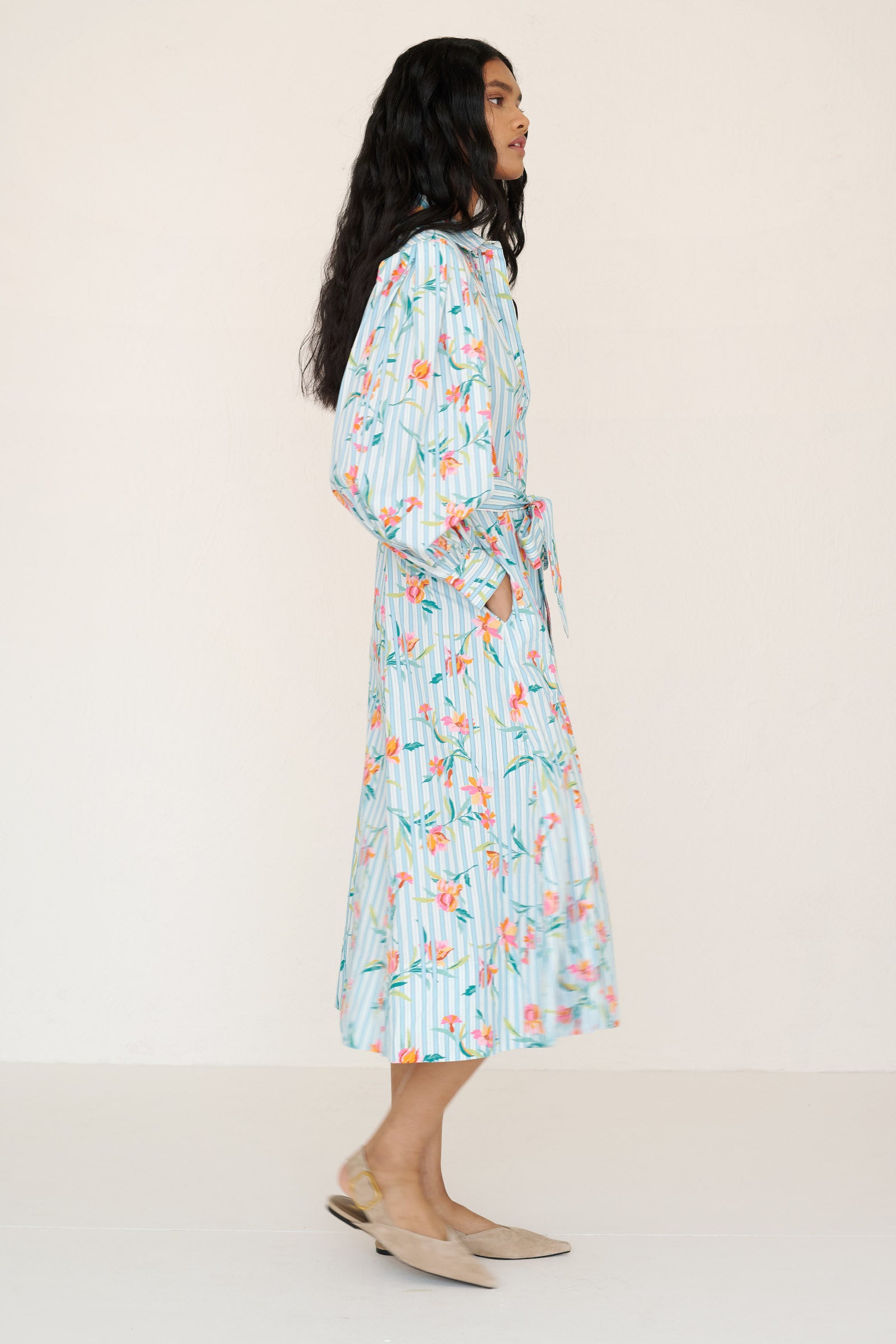 Side view of a woman standing wearing the Harris shirtdress in orchid stripe print. It features a fitted bodice with princess seams, fabric tie belt, flared skirt with godets, and a classic button-front silhouette.