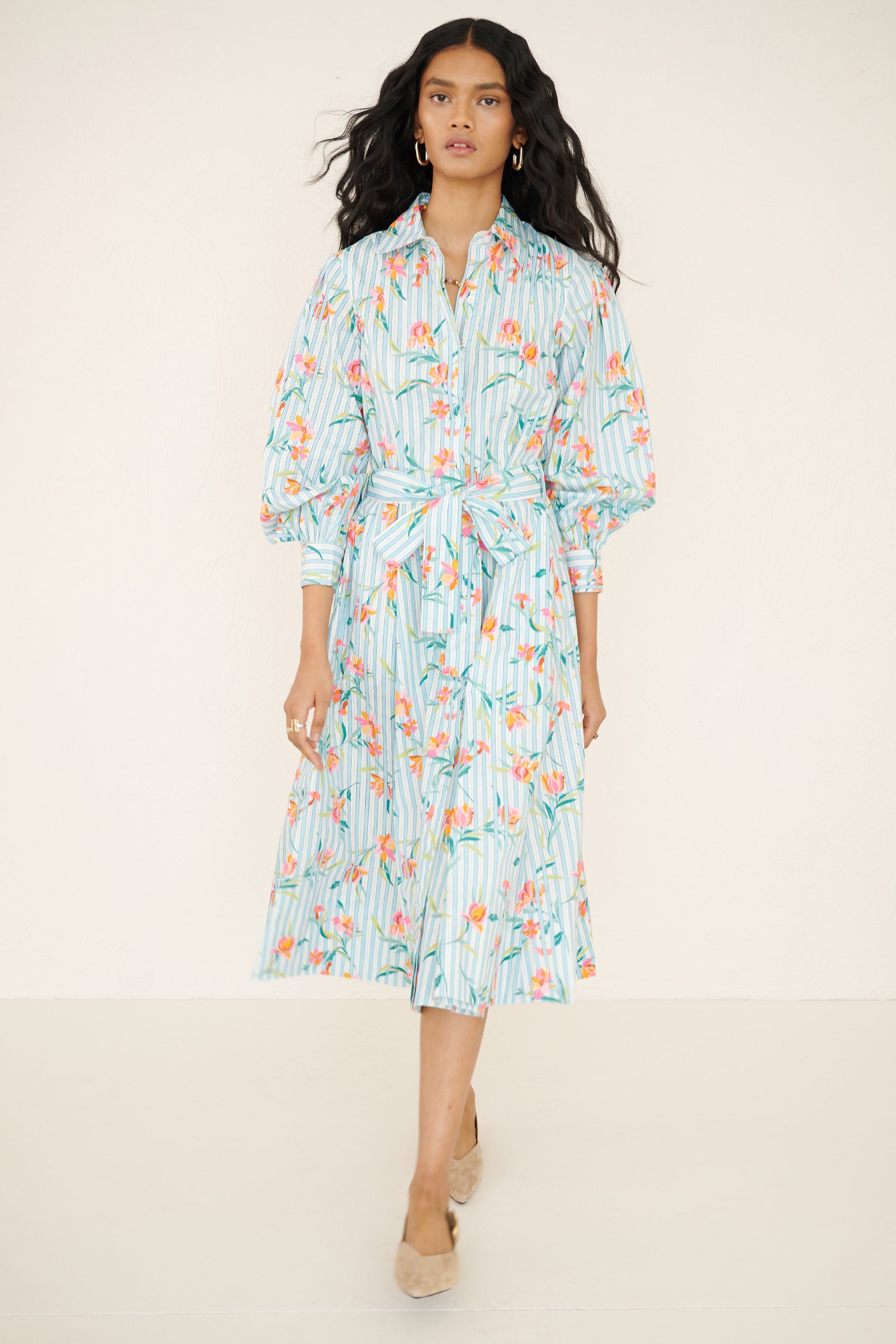 Front view of a woman walking forward wearing the Harris shirtdress in orchid stripe print, featuring a fitted bodice with princess seams, fabric tie belt, flared skirt with godets, and a classic button-front silhouette.