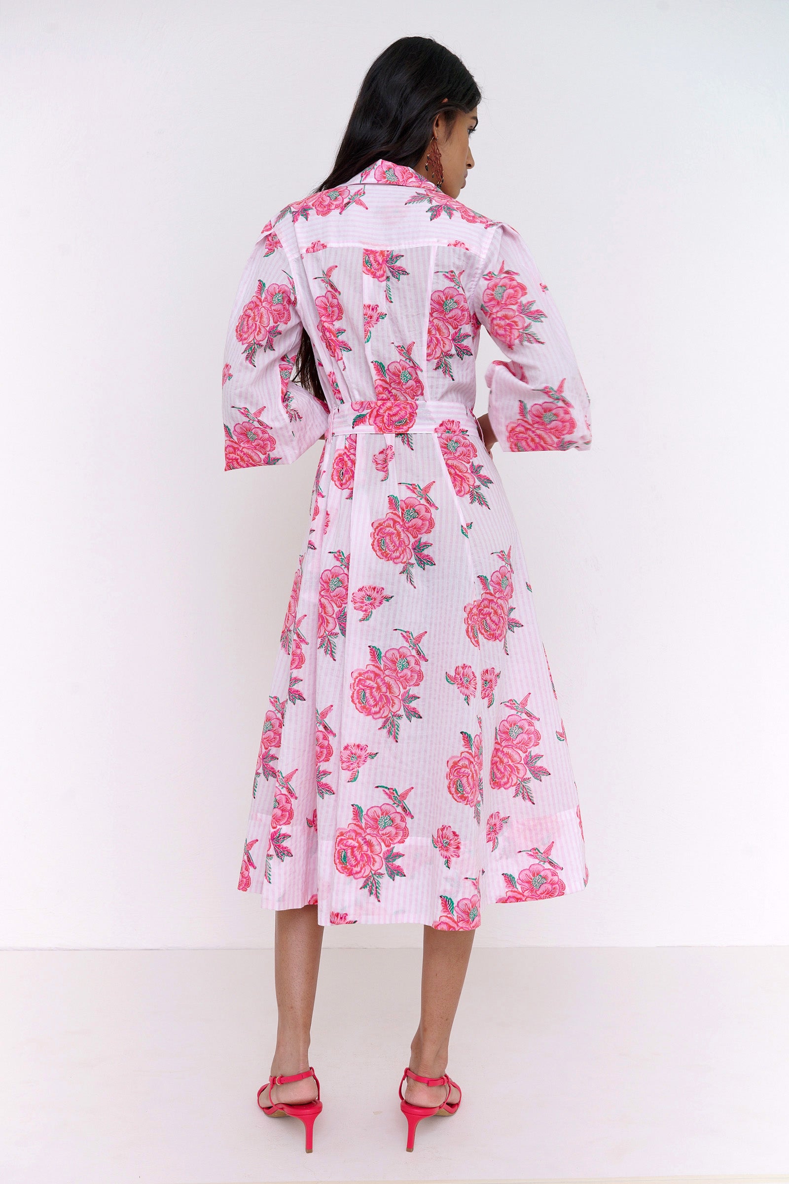 Back view of woman standing . She is wearing the Harris dress in the Eliza Rose print, featuring a fitted shirtdress silhouette, fabric tie belt, flared skirt with godet panels, and hand block-printed floral motifs.