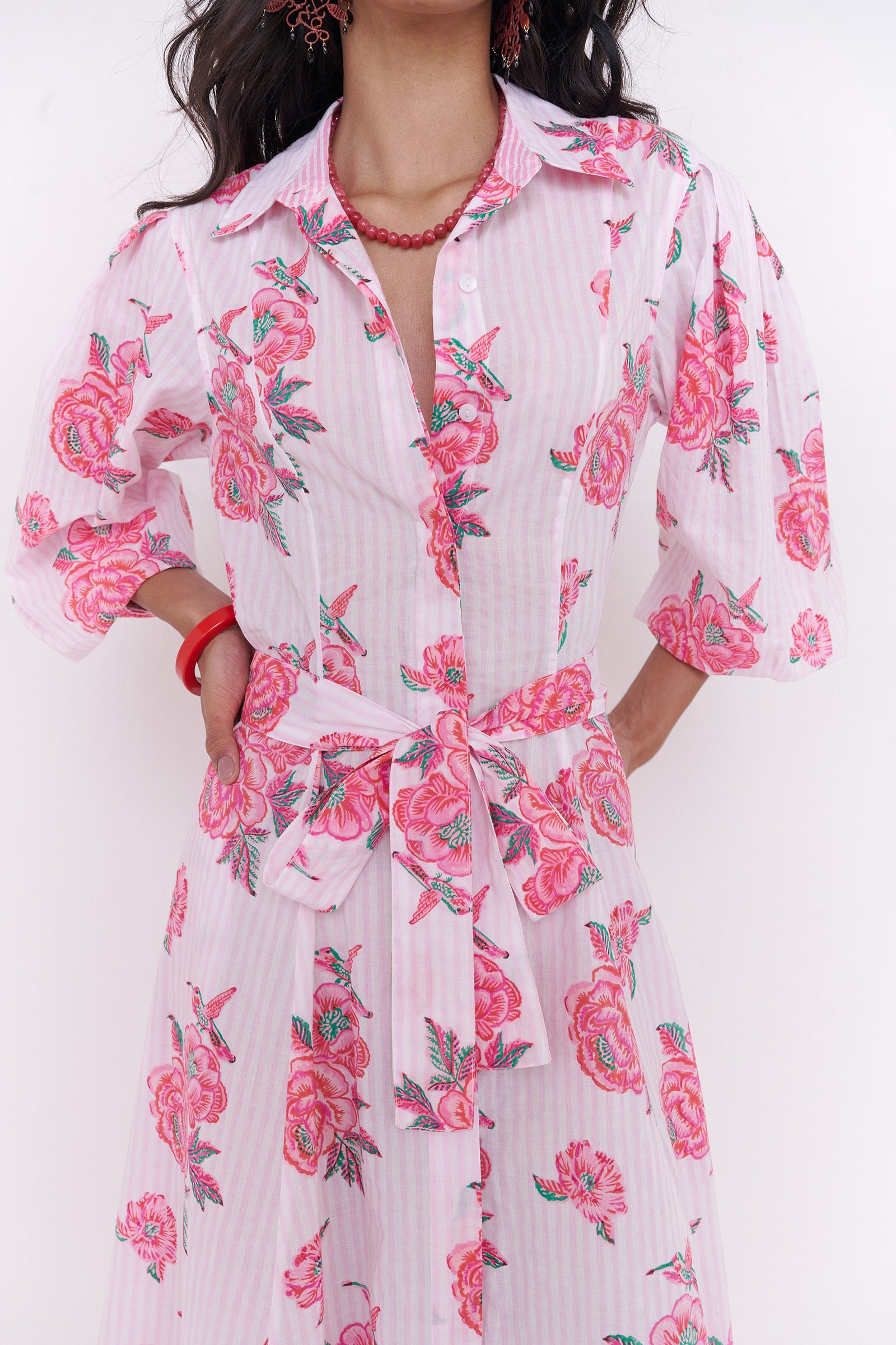 Front view close up of woman standing . She is wearing the Harris dress in the Eliza Rose print, featuring a fitted shirtdress silhouette, fabric tie belt, flared skirt with godet panels, and hand block-printed floral motifs.