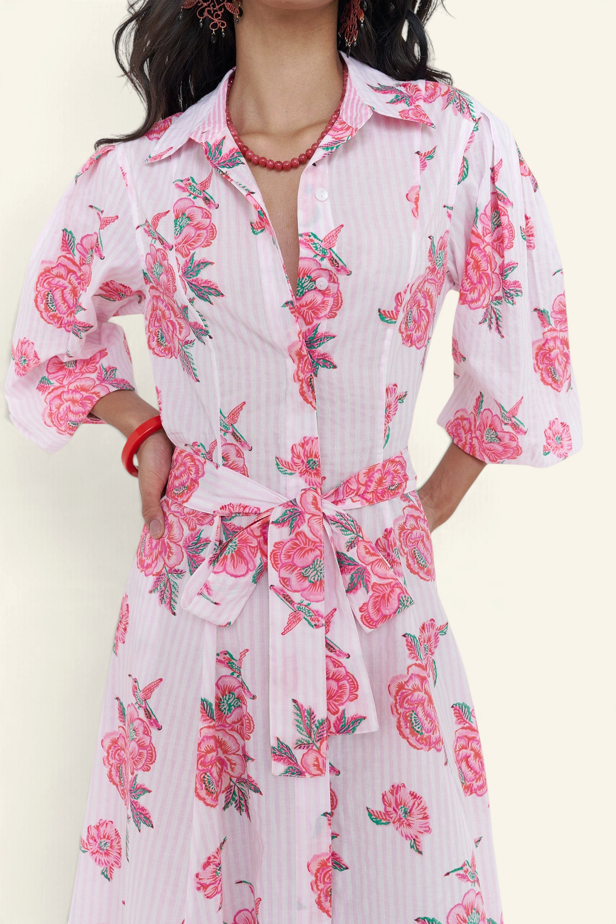A woman wearing a pink and white striped shirt dress with a pink rose floral print, featuring three-quarter sleeves and a matching tie waist belt.