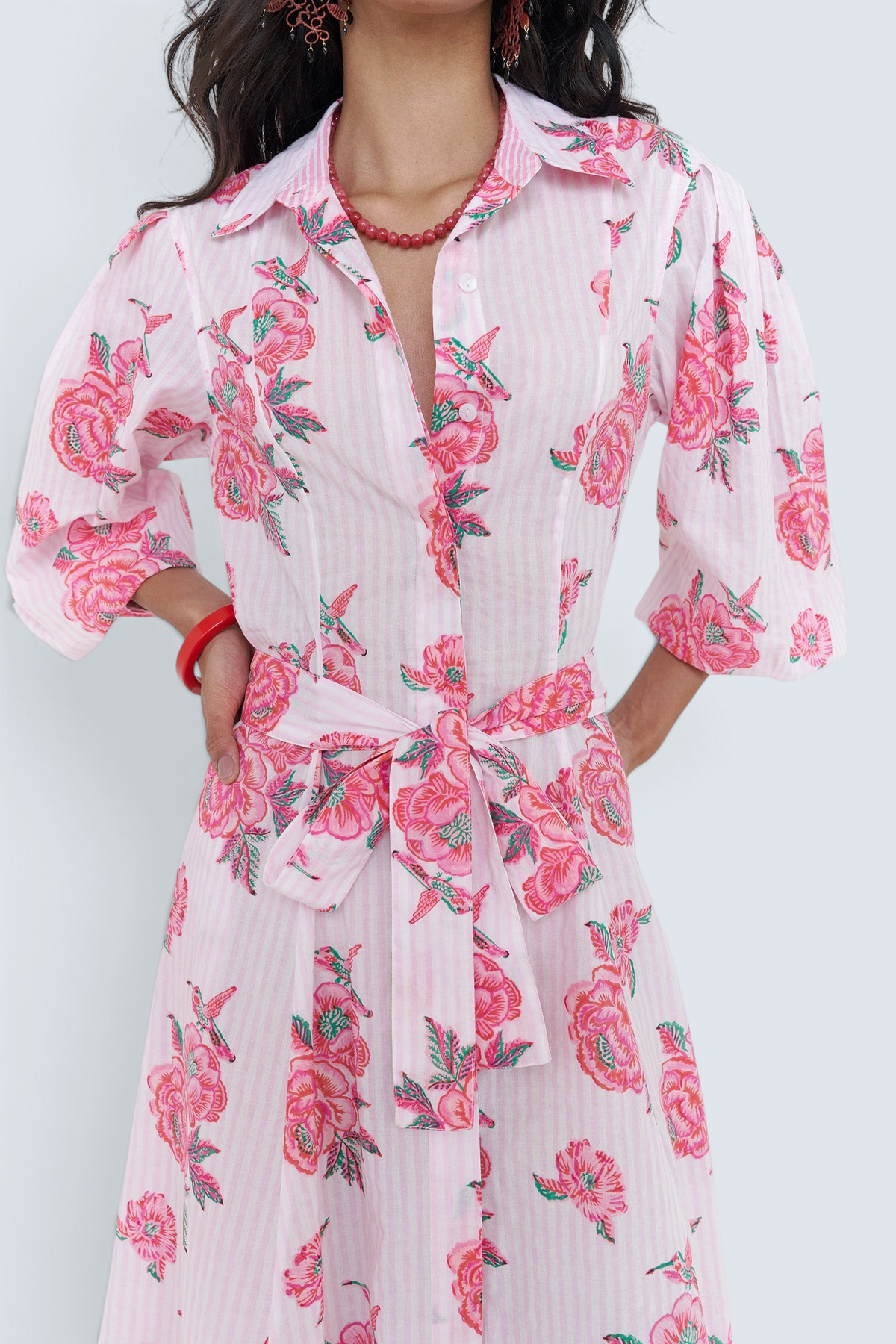 A woman wearing a pink and white striped shirt dress with a pink rose floral print, featuring three-quarter sleeves and a matching tie waist belt.