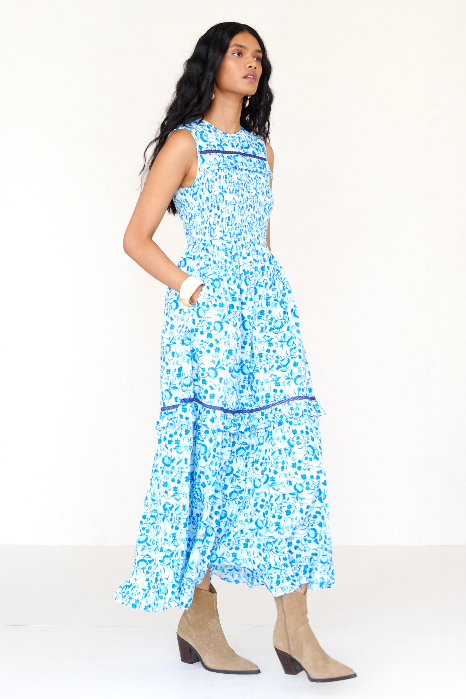 Front side view of a woman standing wearing the Iris dress in Clam Garland print. It features a smocked bodice, tonal lace detailing, keyhole back with loop button and pockets.