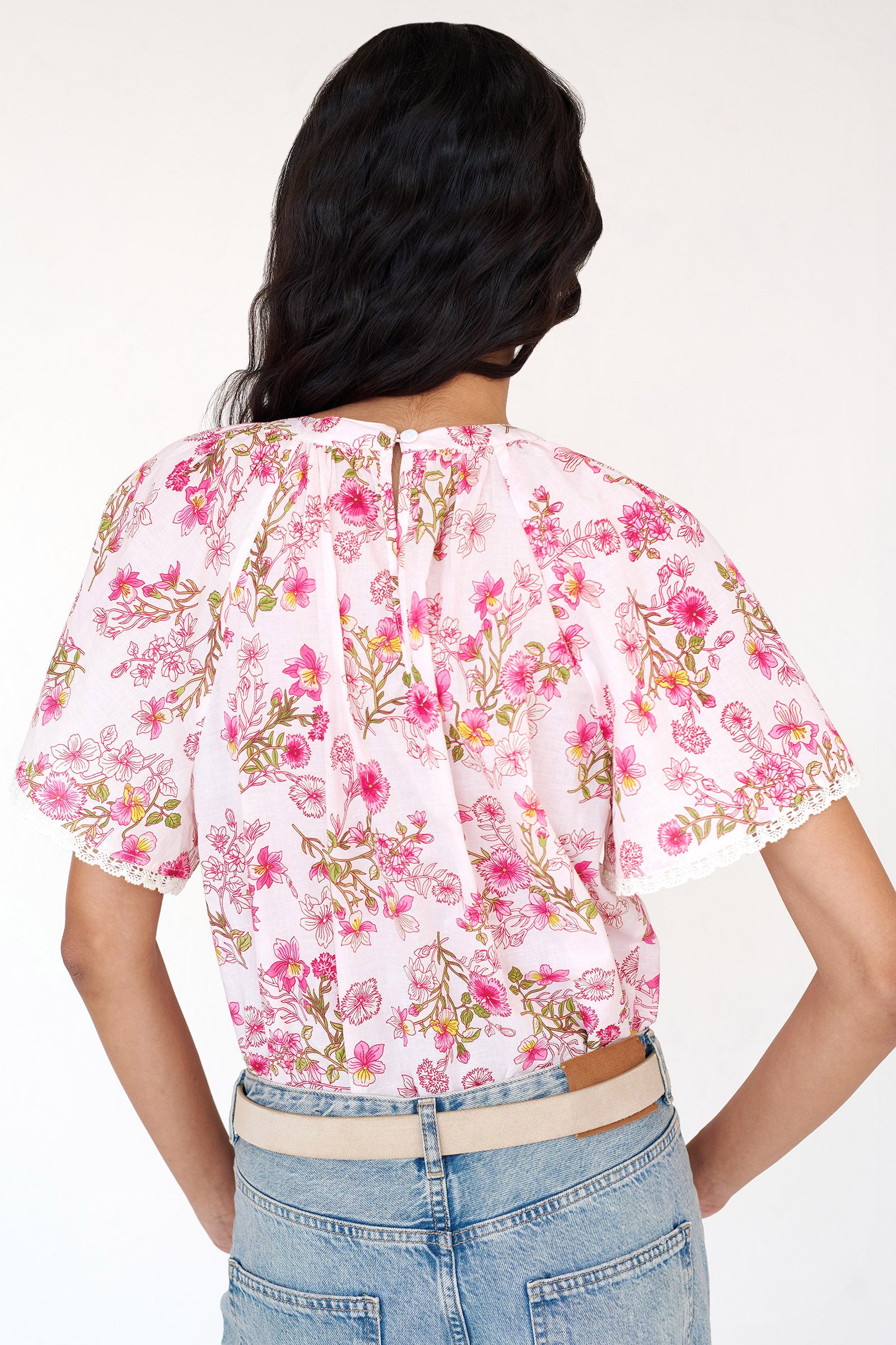 Back view of woman wearing the Joyful top with tucked raglan sleeves, lace trim at the sleeves, and a Burdock wildflower print, finished with a buttoned keyhole at the back neck.
