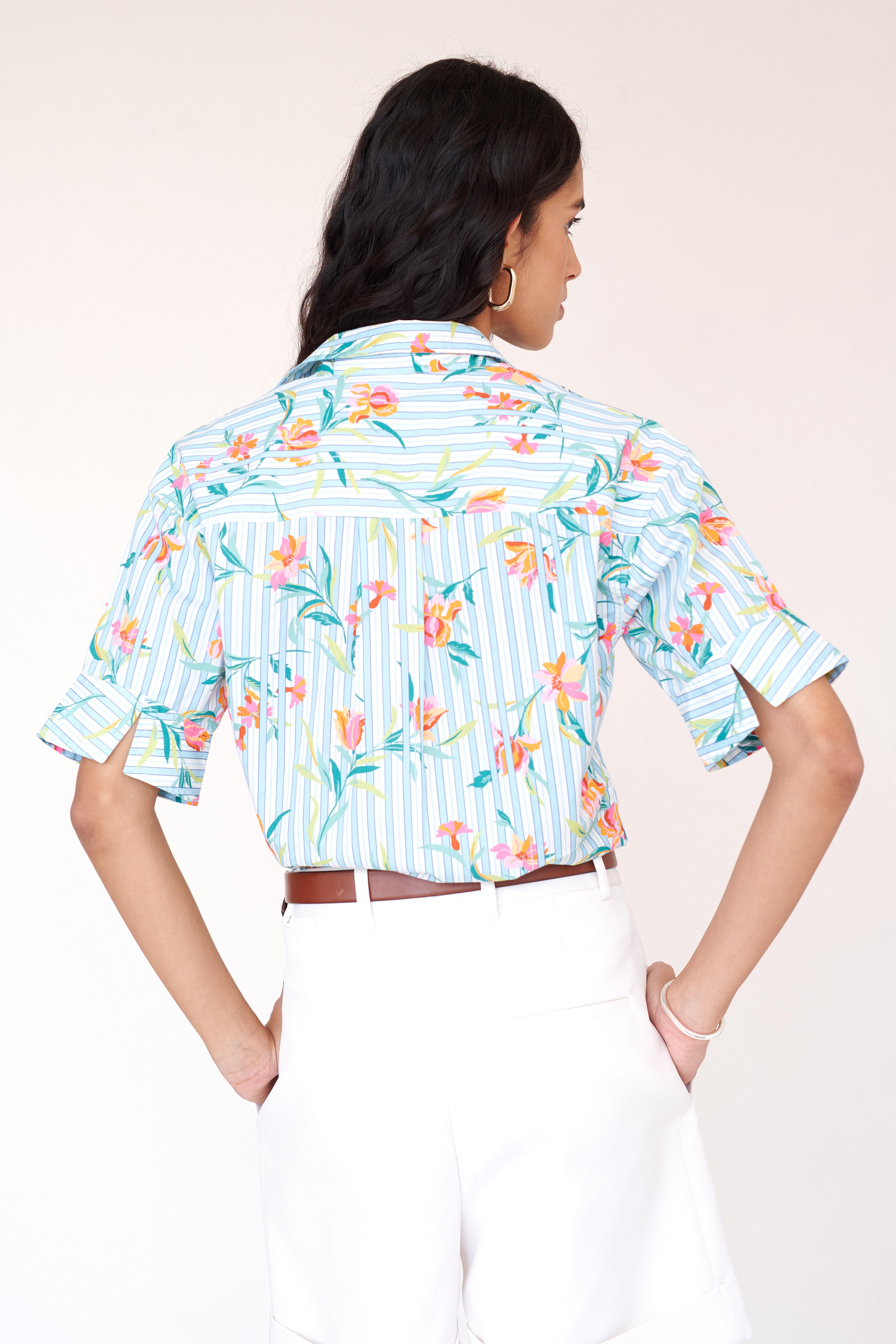 Back view close up of woman wearing the Jura shirt styled with white pants and brown belt. It features a fitted collared shirt with vented cuffs, mixed-direction pinstripes, and delicate orchid motifs.