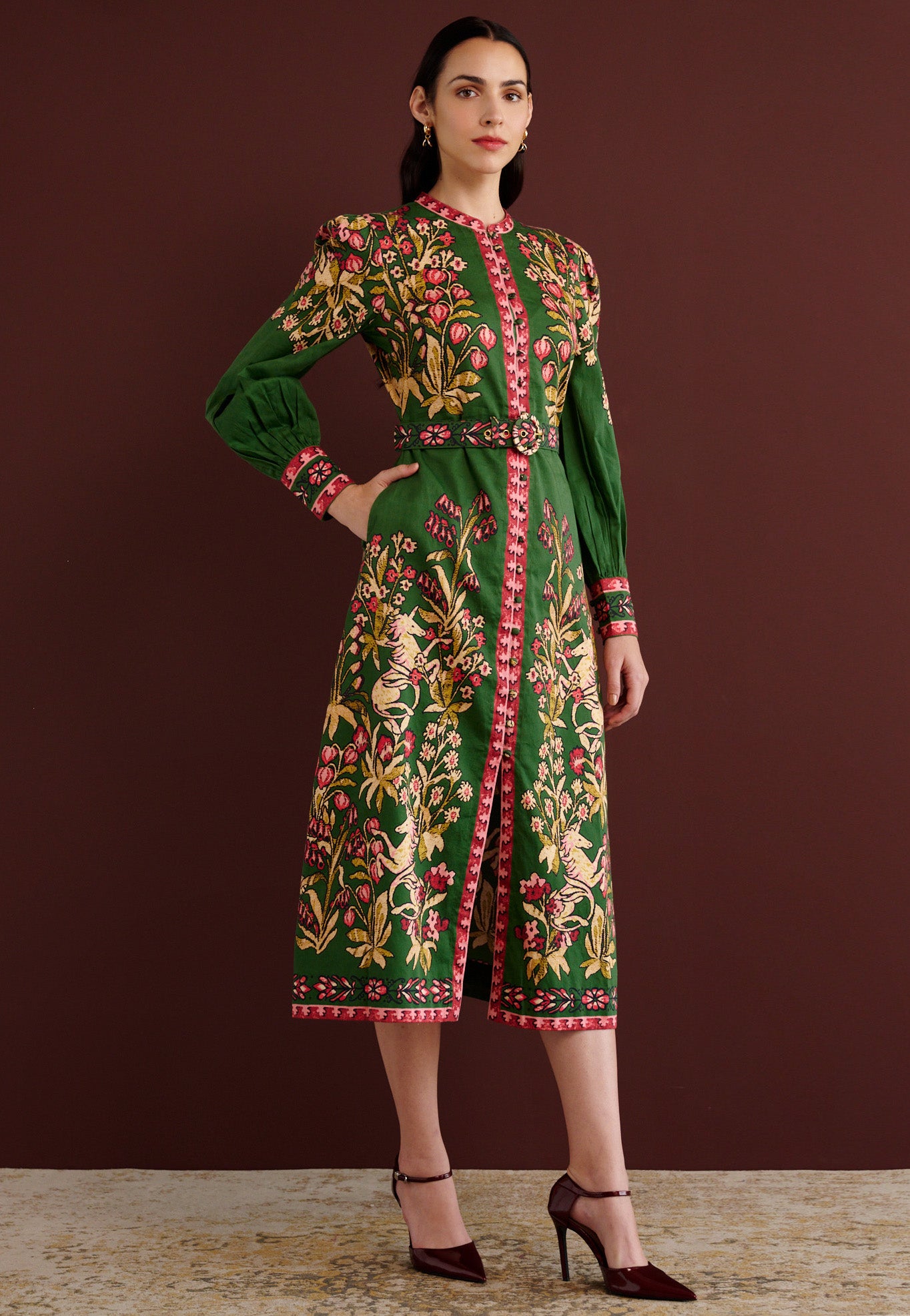 Side view of woman standing with her right hand in pocket. She is wearing the Kay midi dress in Unicorn Tapestry print. It has a fitted bodice, stand collar, fabric-covered buttons, detachable belt, side-seam pockets, and 15th-century-inspired enchanted garden motifs on the shoulders and skirt.